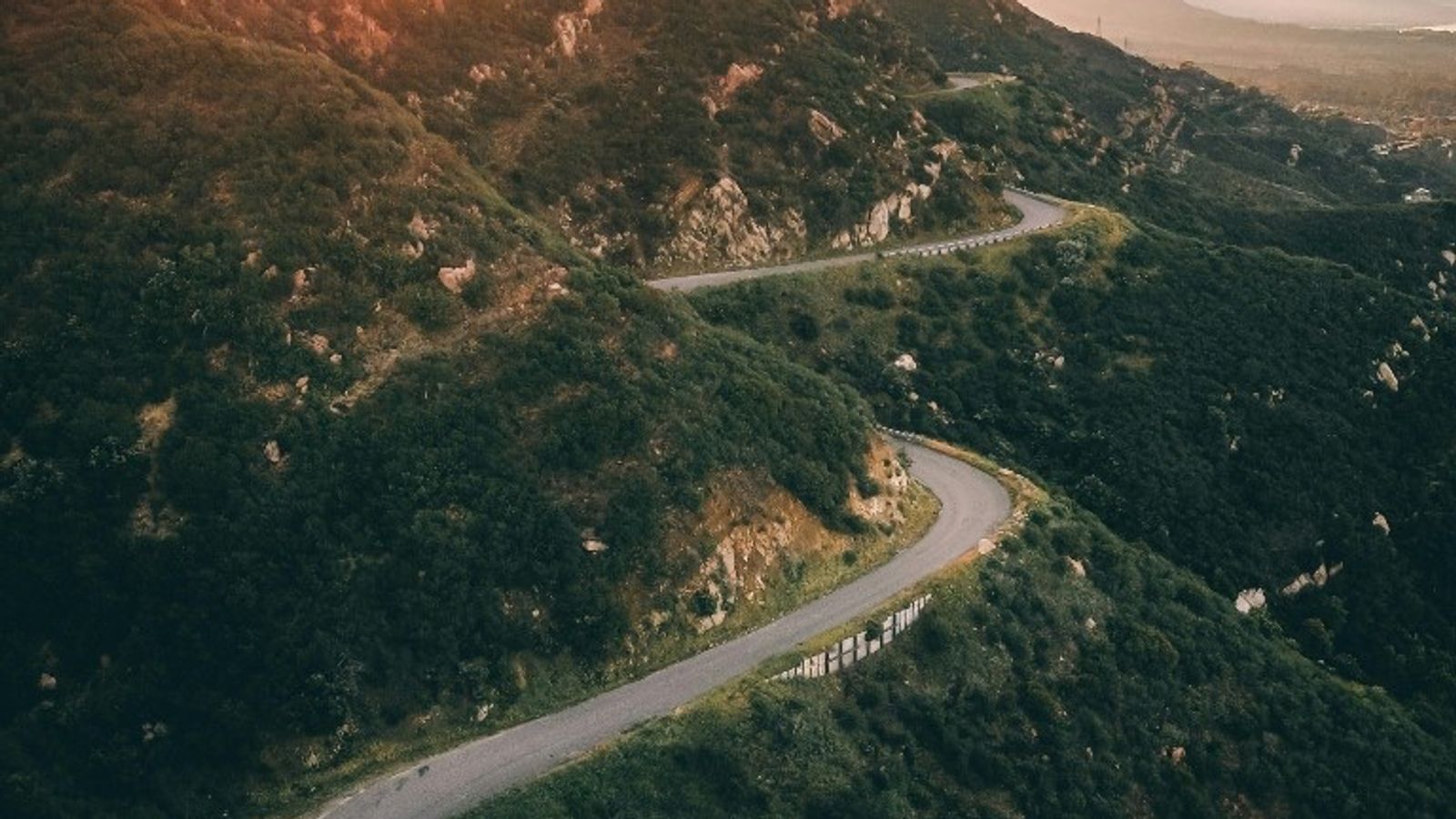 A winding mountain road at sunset disappearing into the hills, symbolizing steady progress through a step-by-step process