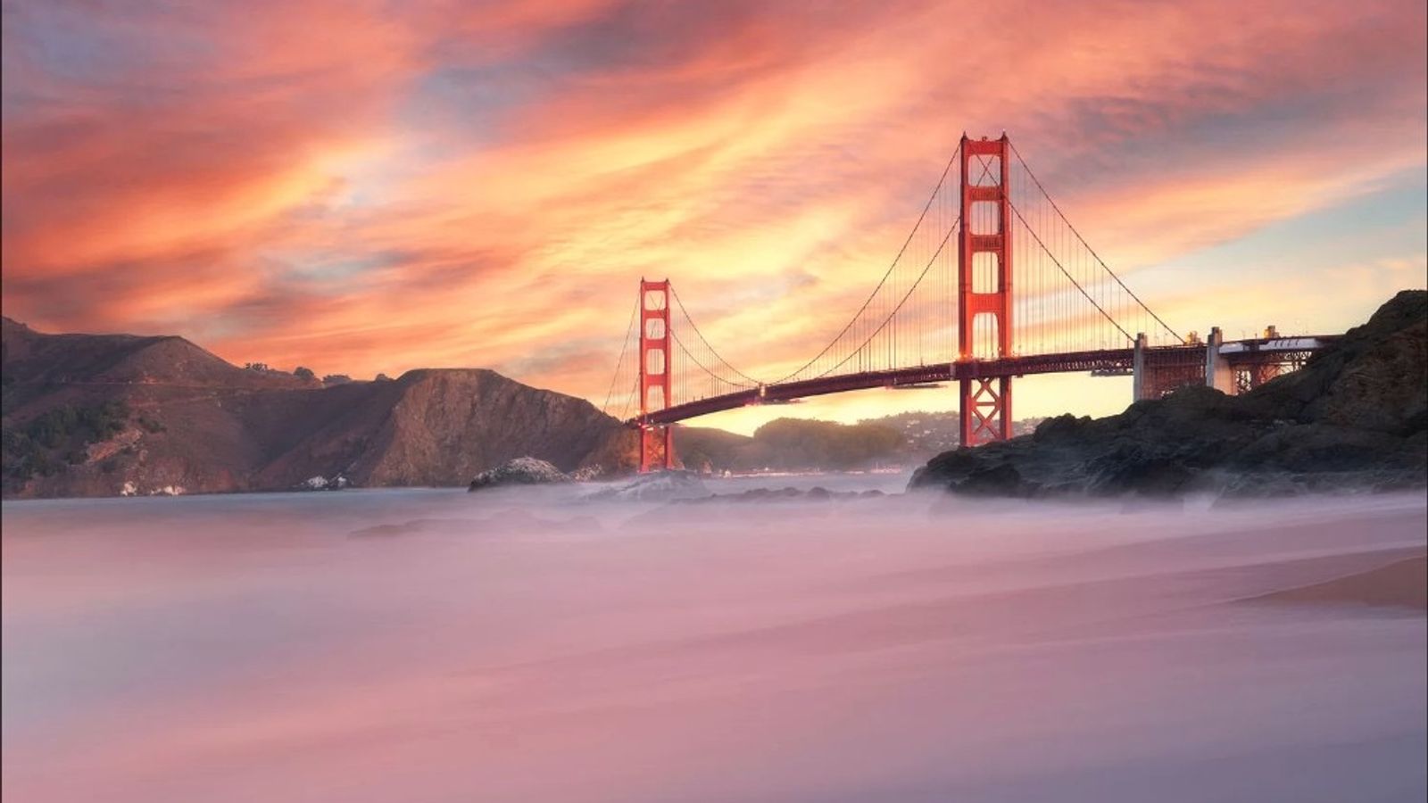 Golden Gate Bridge at sunset with vibrant orange and pink clouds and misty water