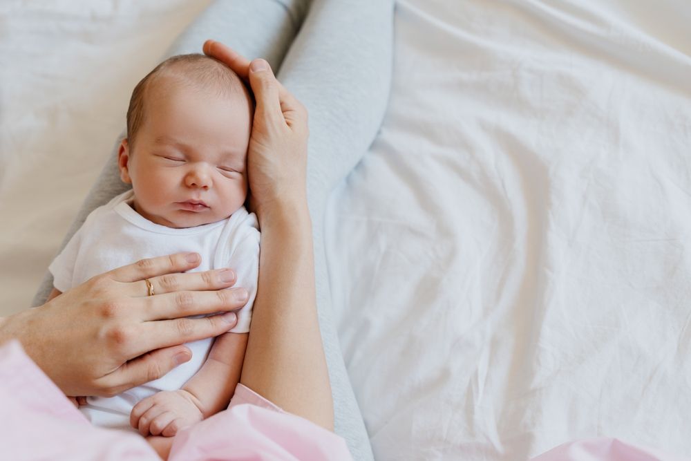 Mother cradling a sleeping newborn in bed, showing postpartum care and concerns about hospital monitoring for mom and baby in New Jersey.