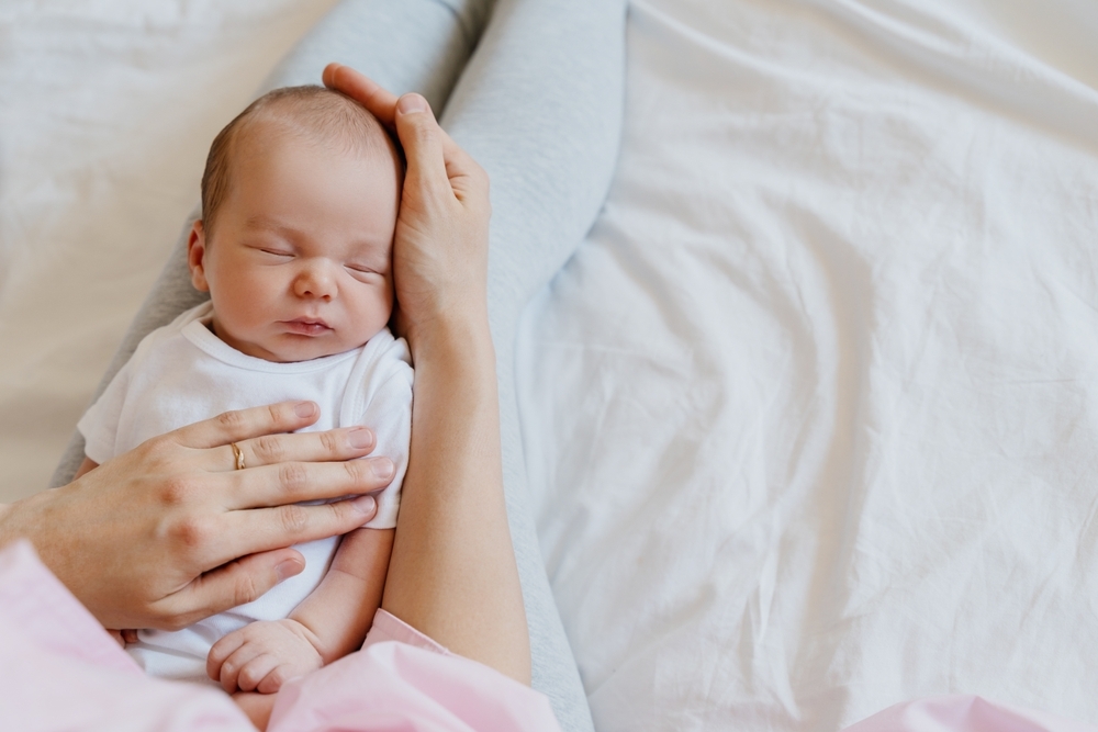 Image Mother cradling a sleeping newborn in bed, showing postpartum care and concerns about hospital monitoring for mom and baby in New Jersey.