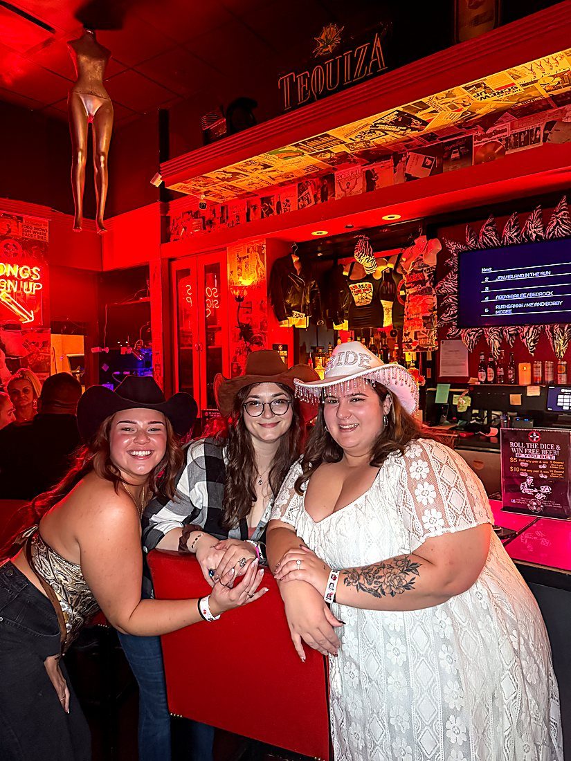 Three friends in cowboy hats celebrating at the red bar