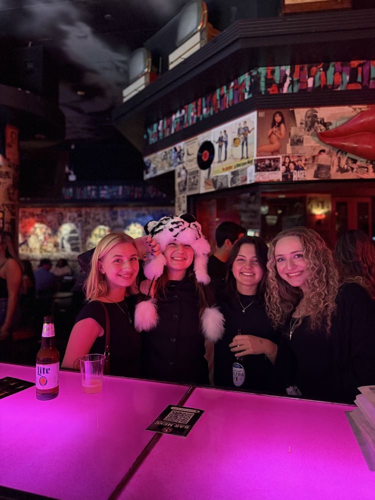 Four friends posing at the pink bar, one in a fuzzy hat