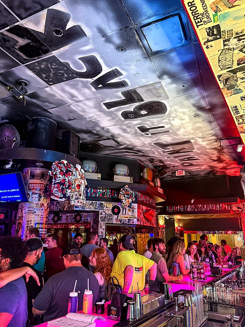 A busy night along the pink bar under the black-lettered ceiling