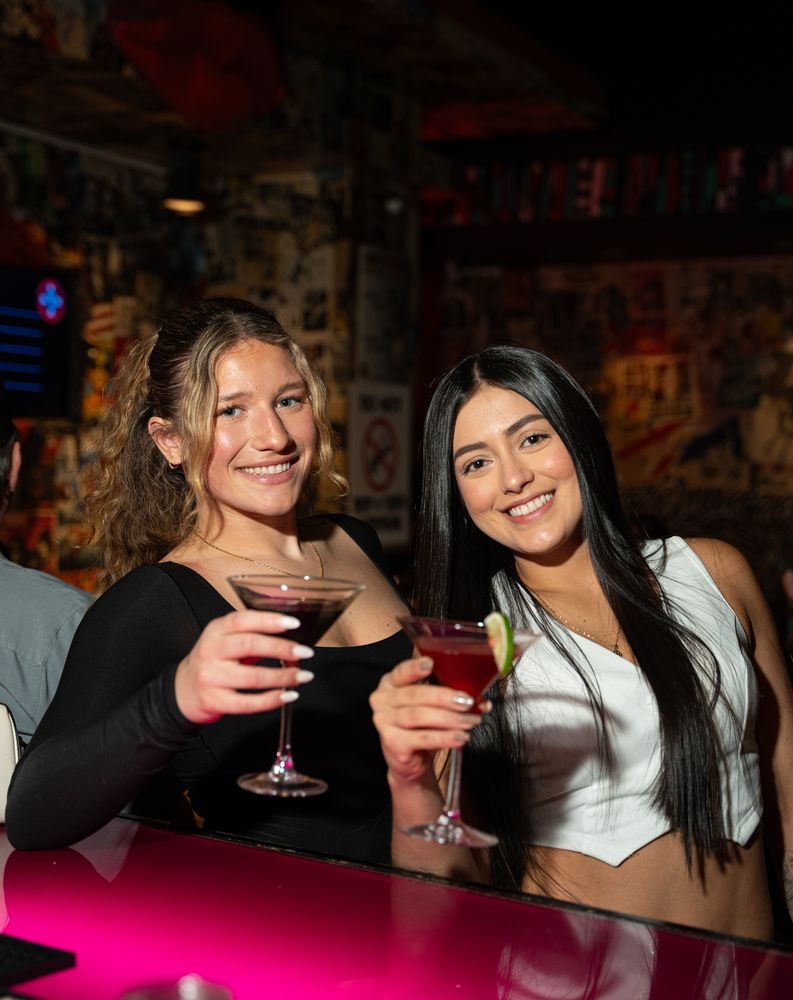 Two friends raising cocktails at the bar