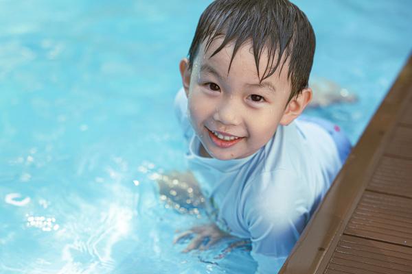 Anak laki-laki tersenyum di tepi kolam renang