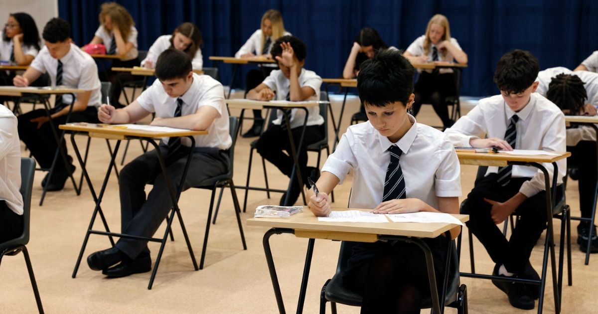 A student sitting at a desk in a quiet classroom concentrating on an academic examination paper
