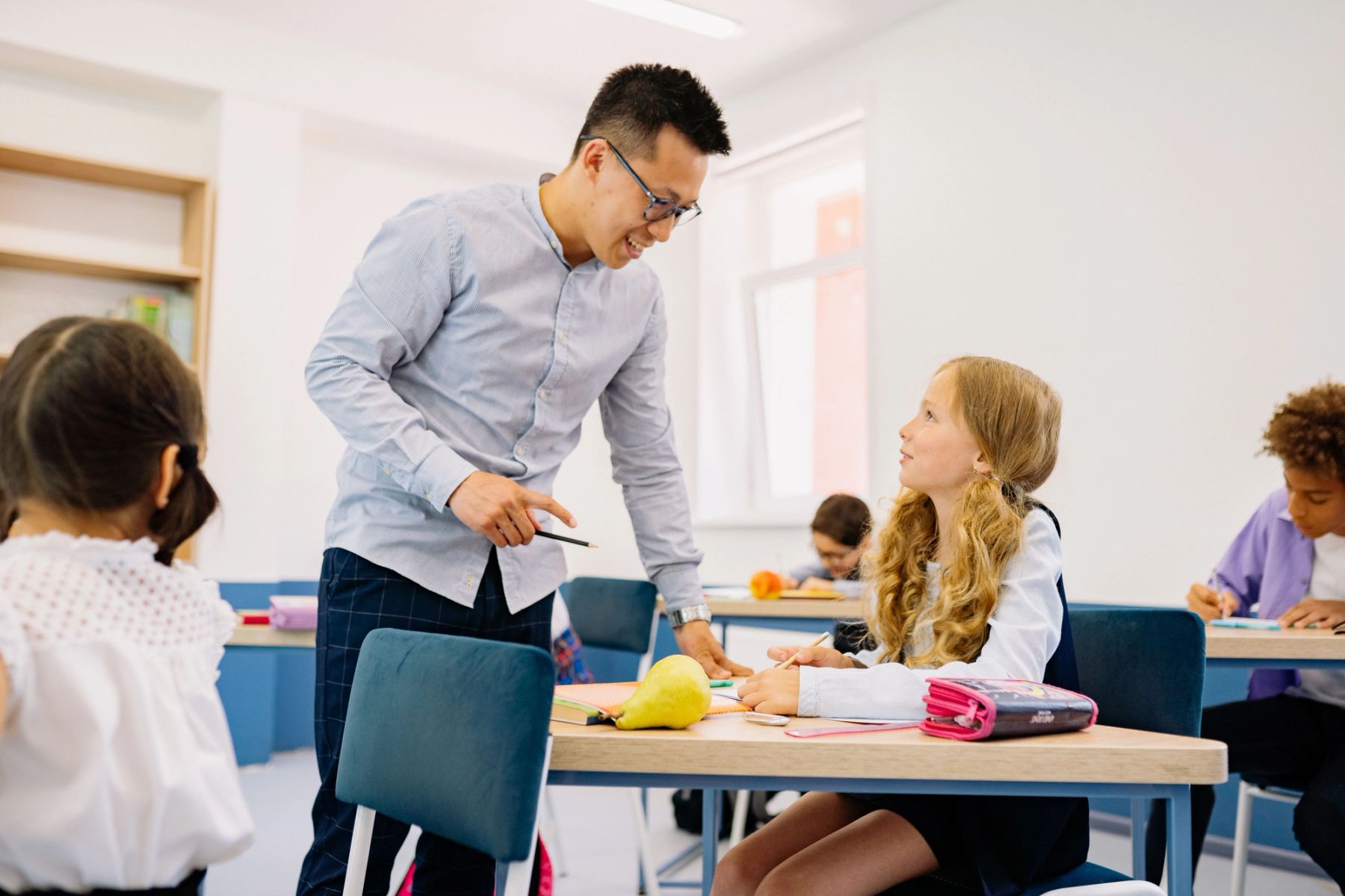 Teacher working individually with a student at a desk in a classroom setting