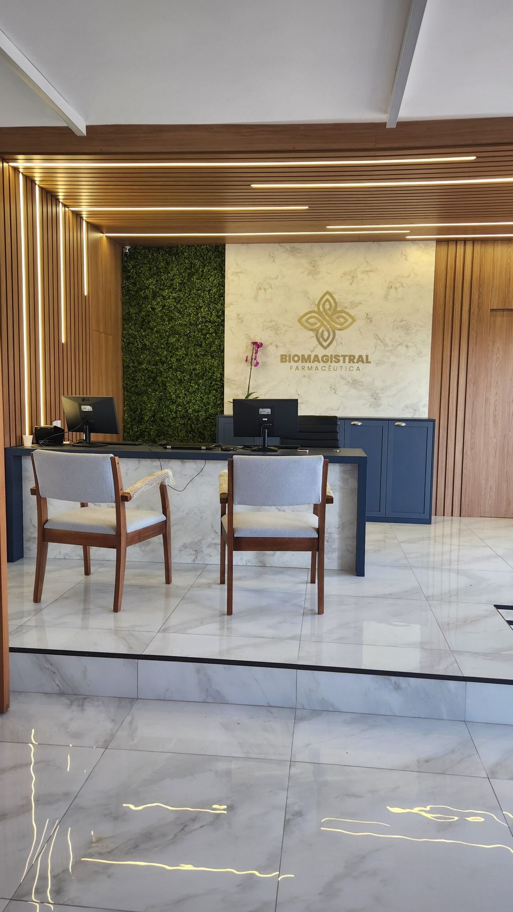 Balcão de atendimento da farmácia com cadeiras e o jardim vertical ao fundo