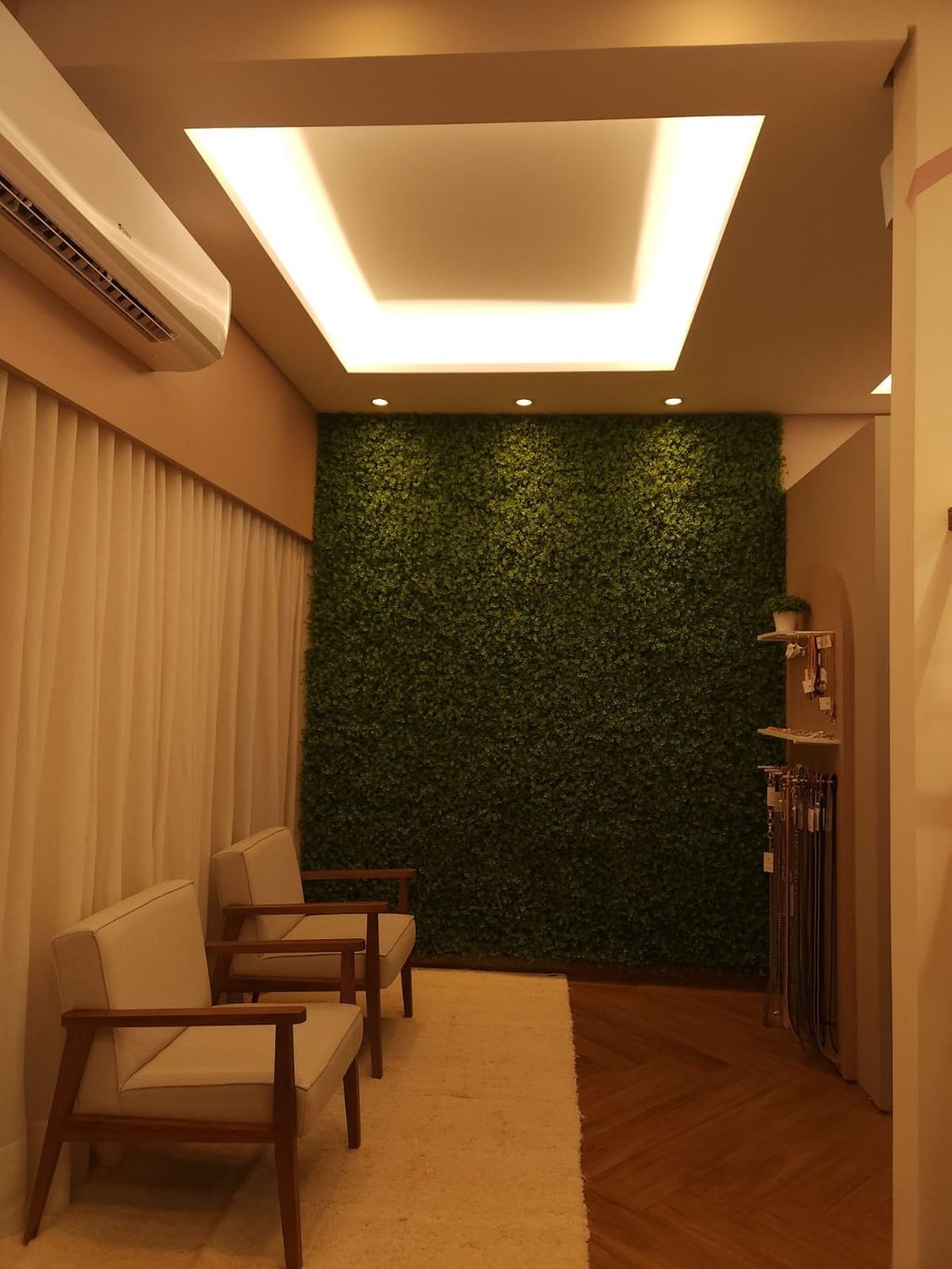 Vista frontal do provador, com a parede verde iluminada pela sanca de luz e duas poltronas