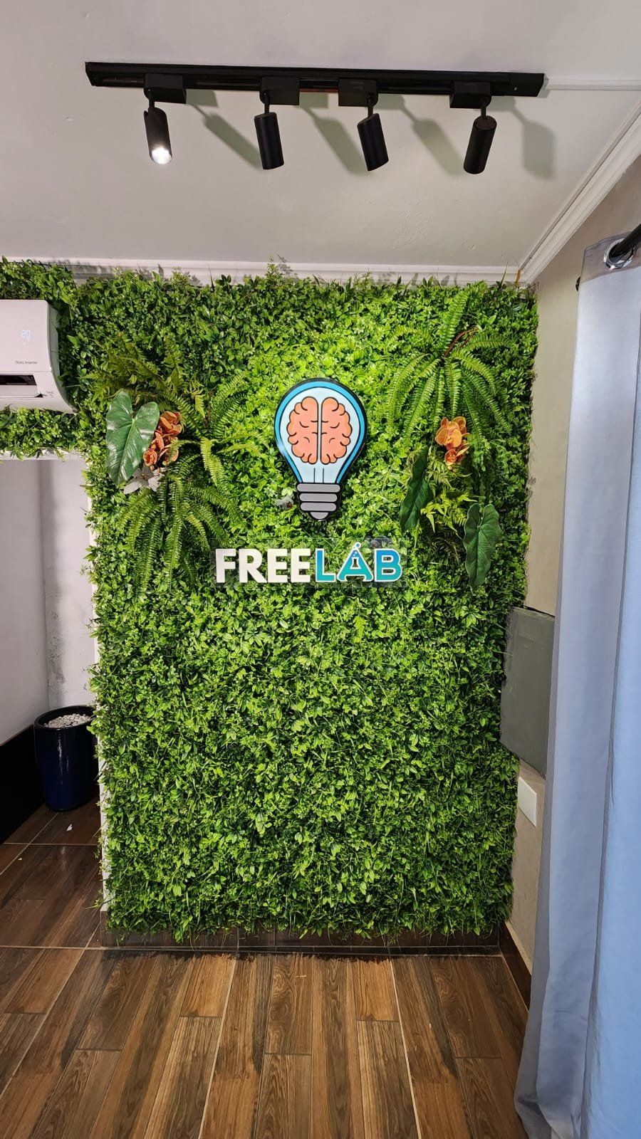 Parede verde com o logotipo iluminado da Free Lab, sob trilho de spots