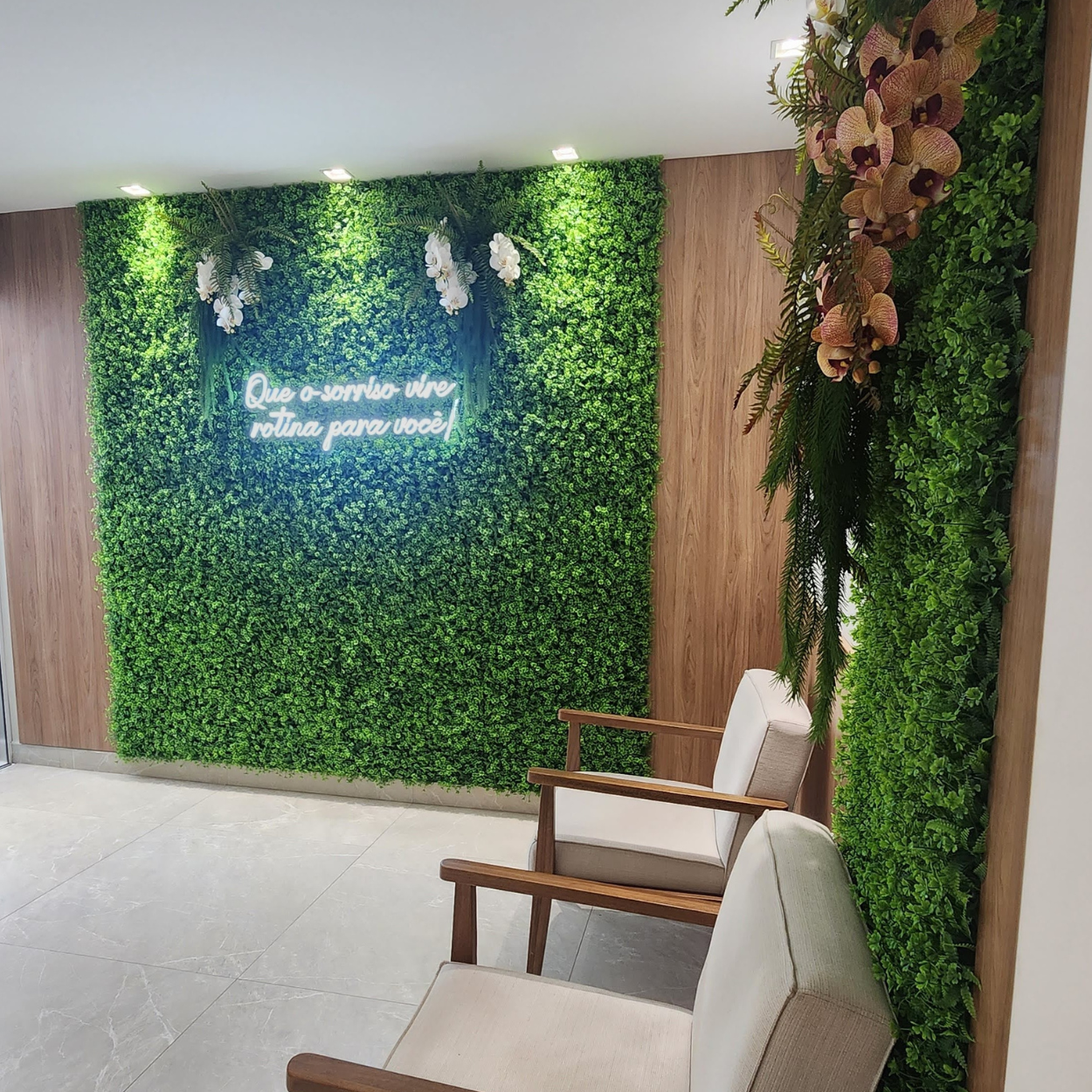 Recepção da AP Odontologia com parede verde, neon "Que o sorriso vire rotina para você!" e orquídeas