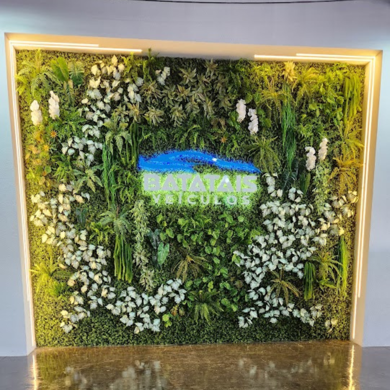 Painel verde com flores brancas e o letreiro da Batatais Veículos no centro, emoldurado por luz