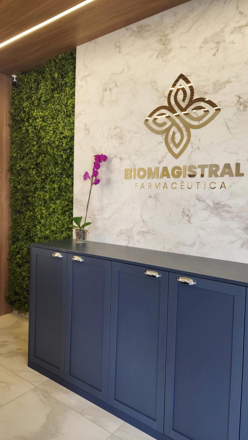Recepção da Farmácia Biomagistral com jardim vertical ao lado do painel de mármore com o logotipo