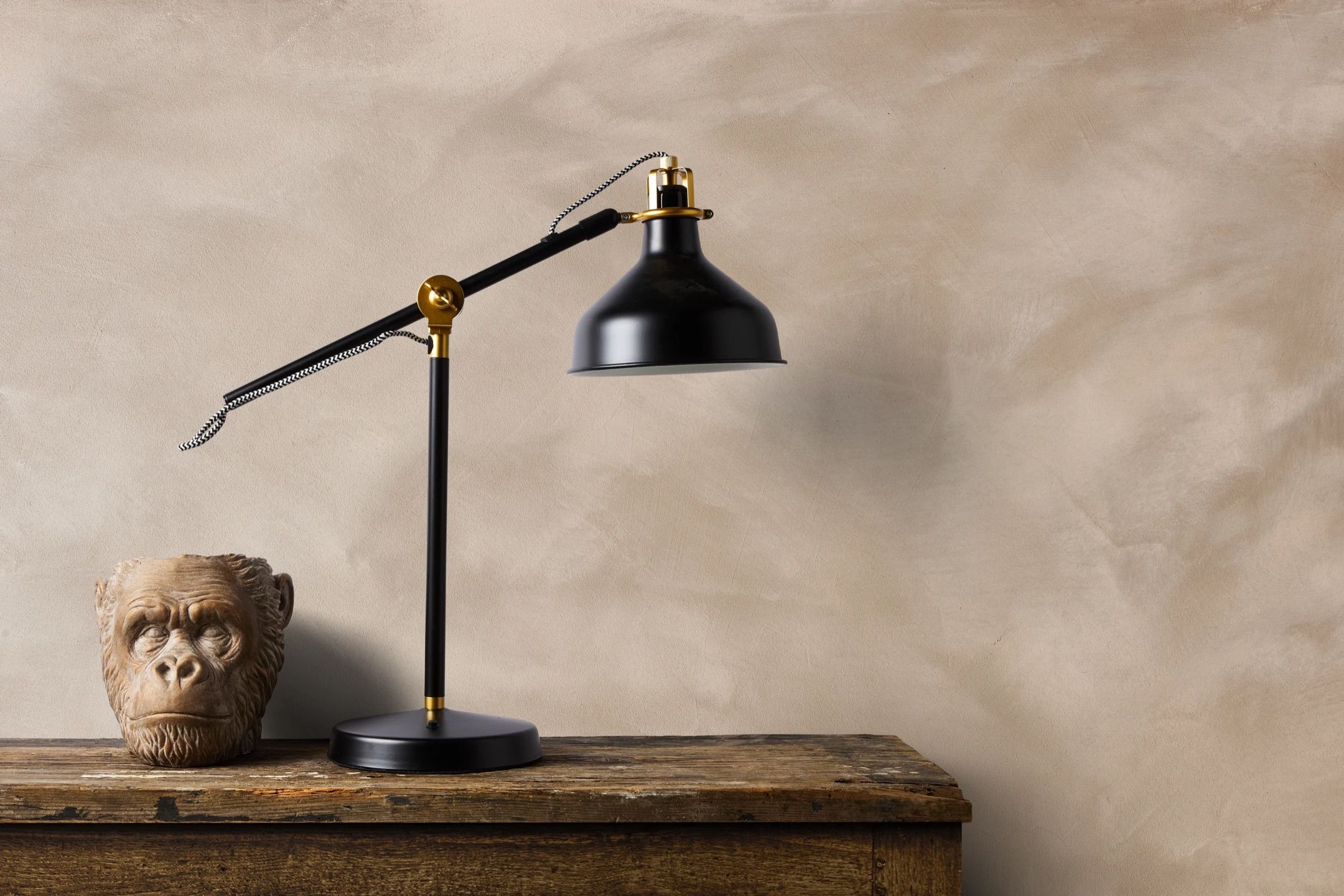 Microcement wall in a warm neutral tone behind a black task lamp and a stone bust