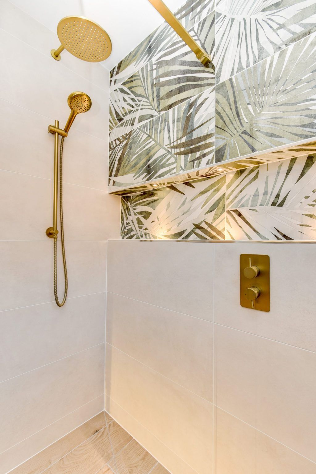 A close-up of a brass shower fitting against a botanical-tiled wall