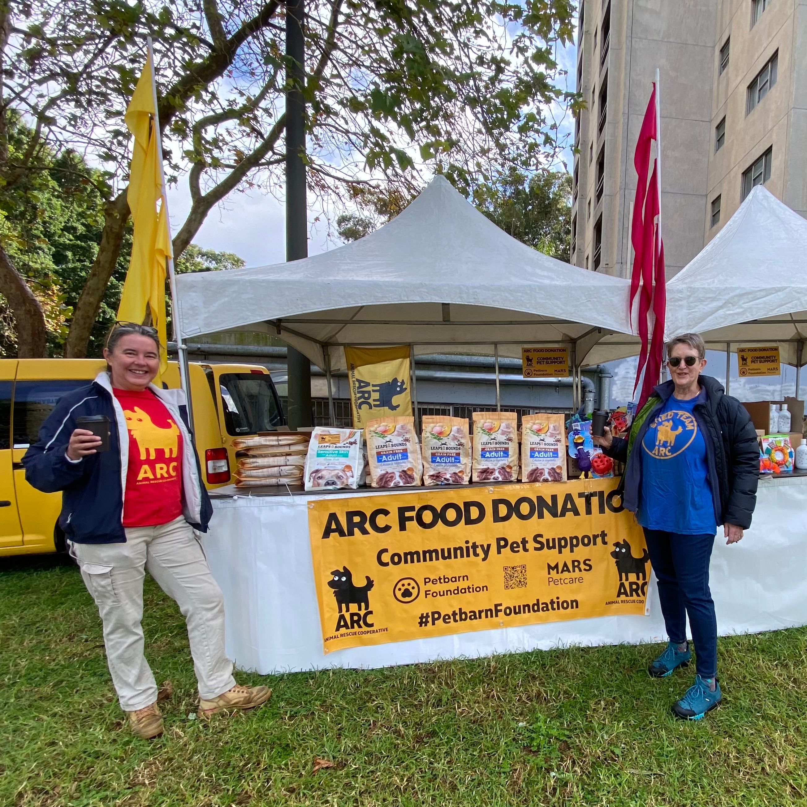 two ladies standing outside arc food donation stand