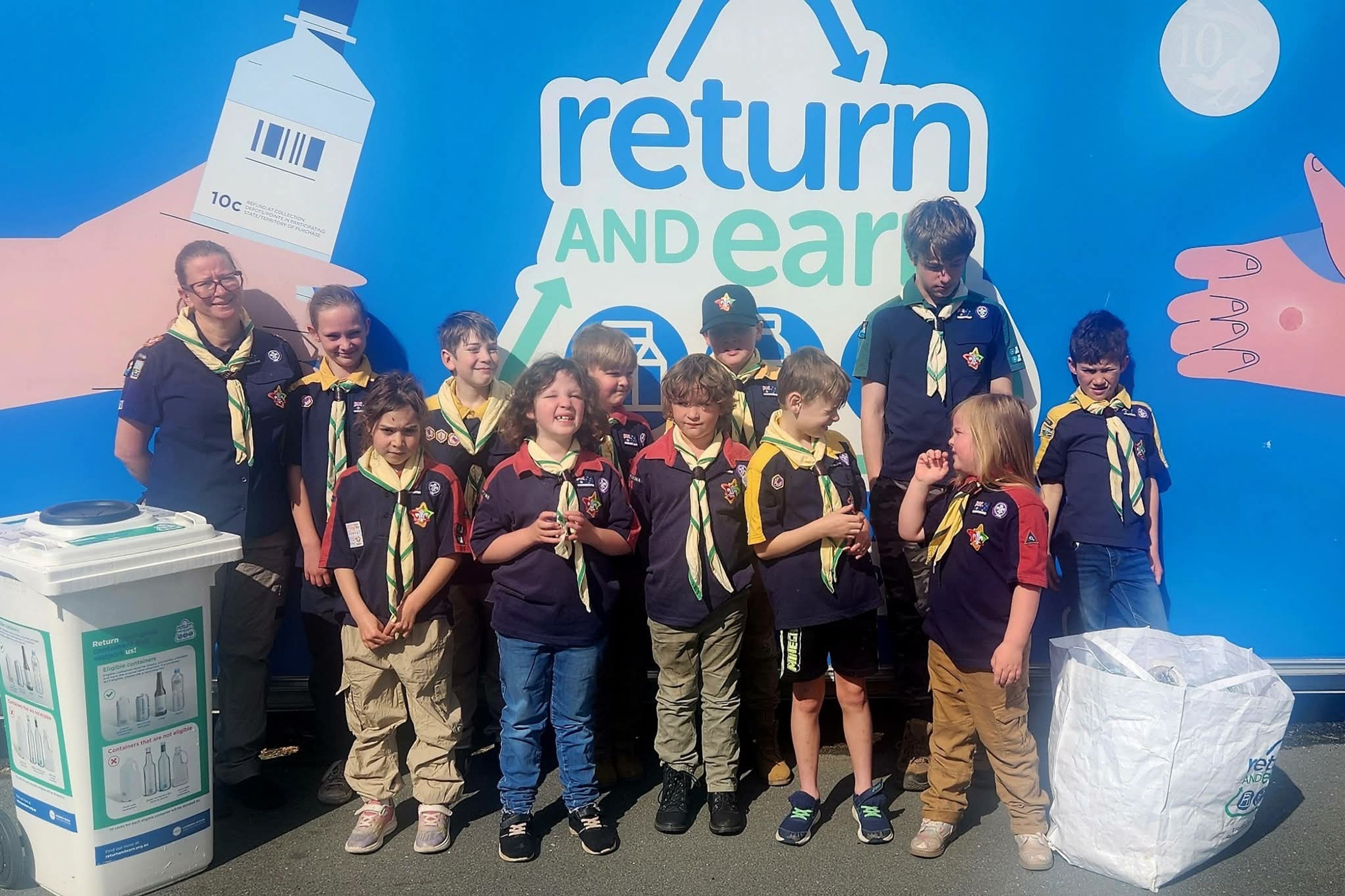 1st cooma scouts taking a photo in front of a return and earn backdrop, with their collected containers