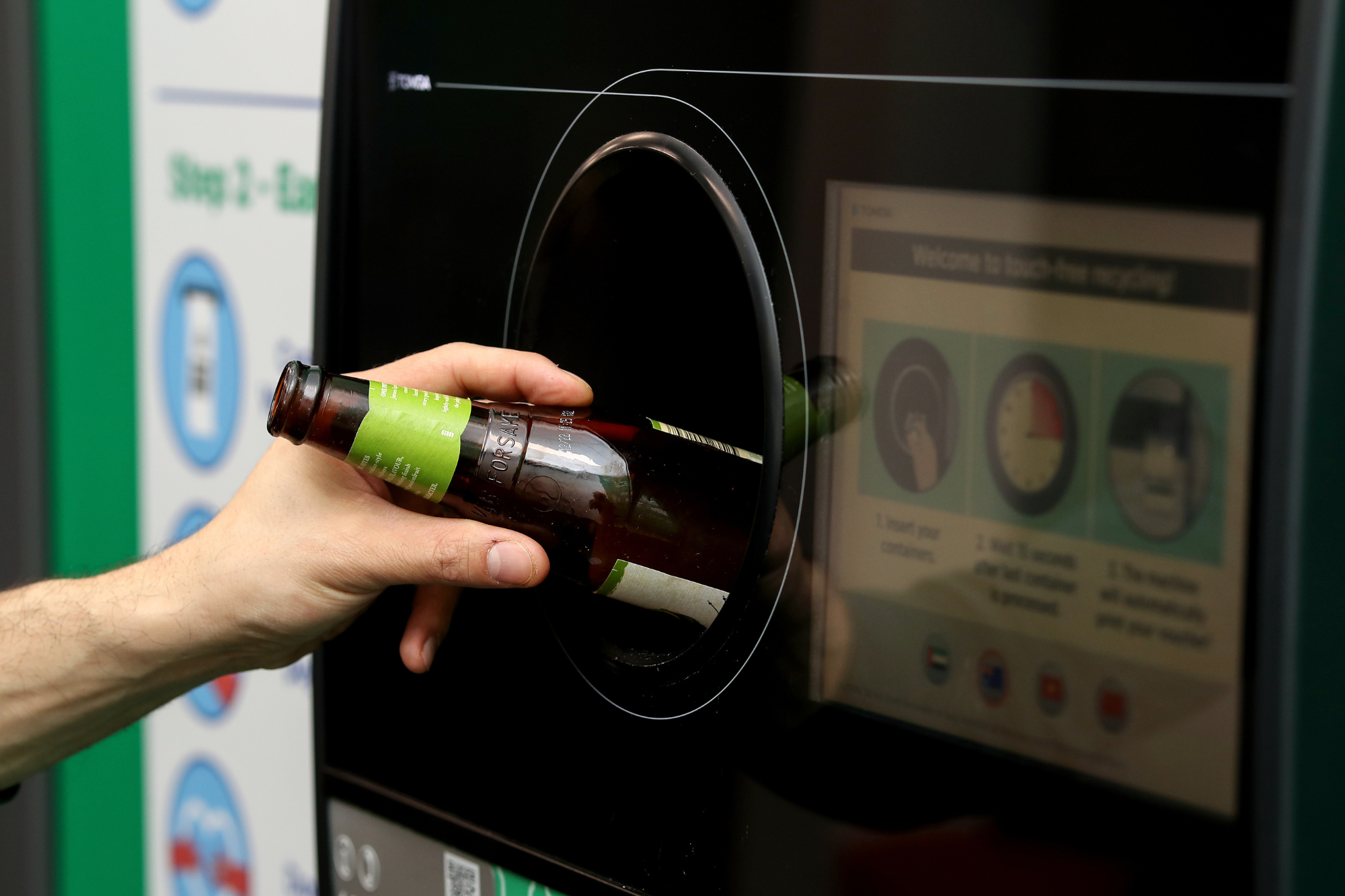 Glass bottle being placed into Return and Earn machine