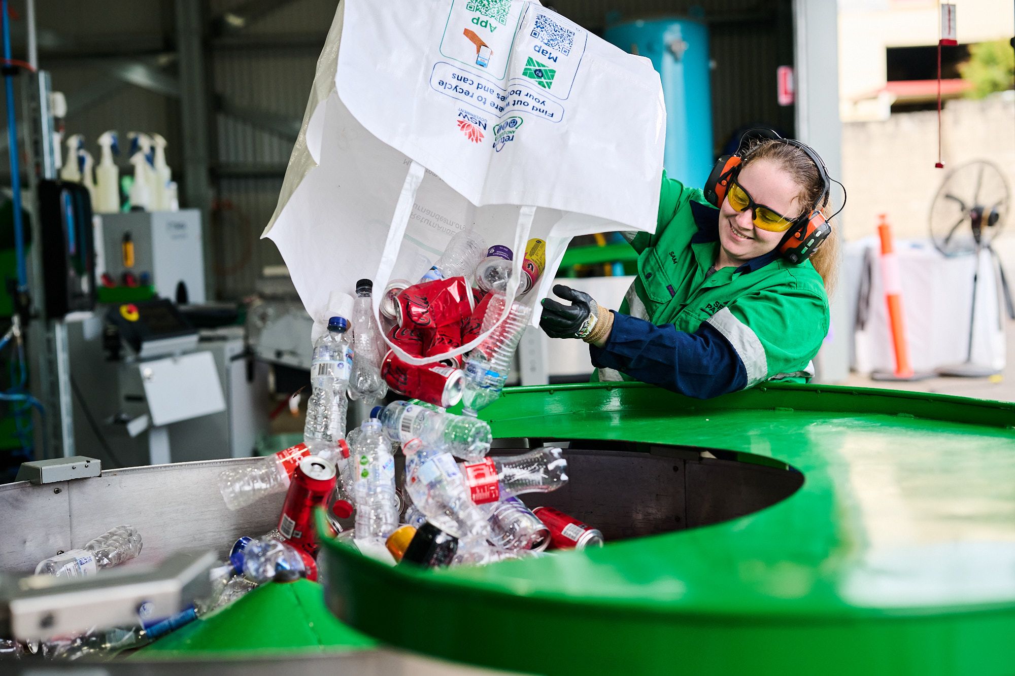 A Return and Earn depot employee tipping a bag of eligible containers into a singulator to be counted.