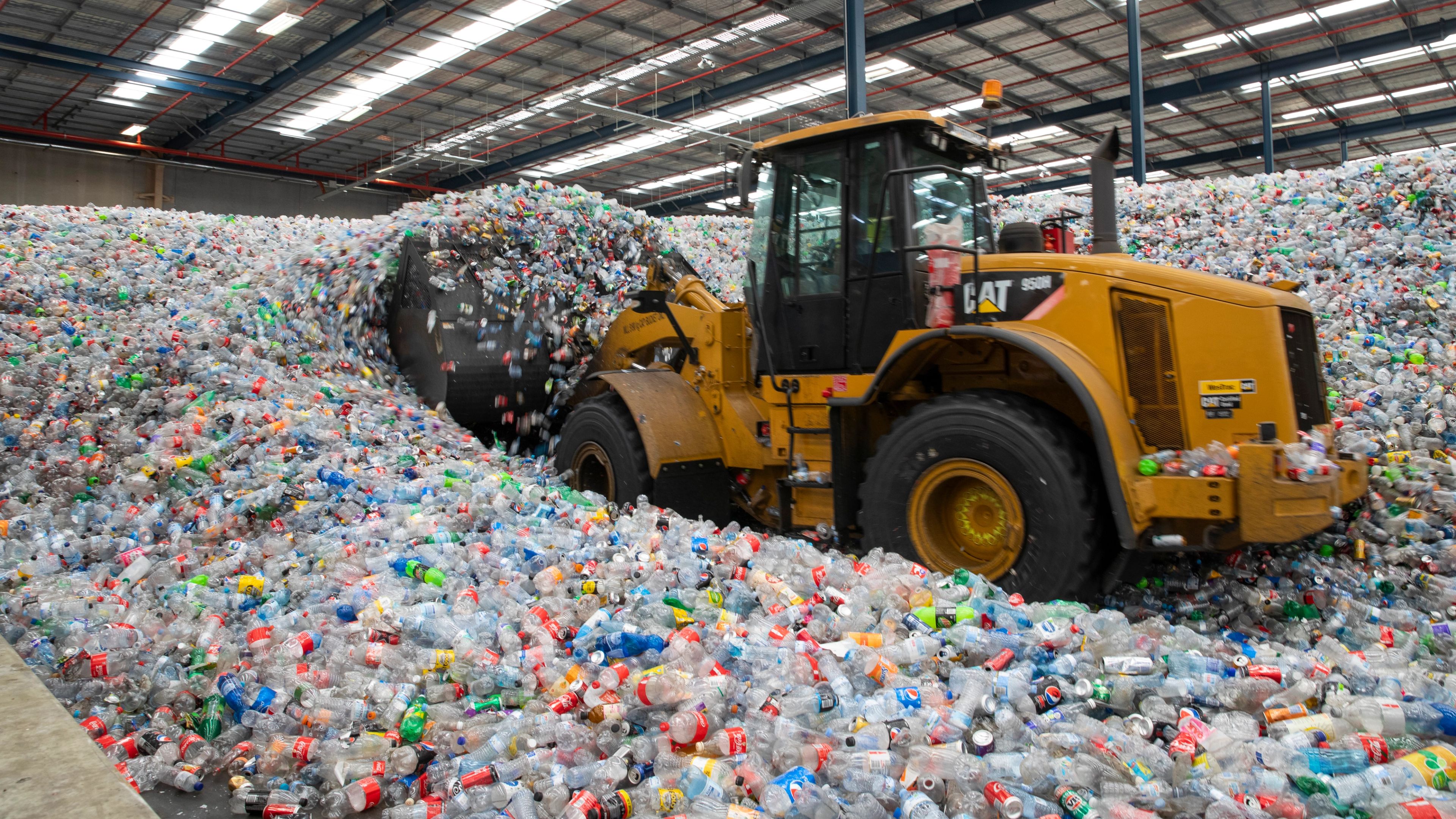Digger pushing containers and bottles at sorting facility