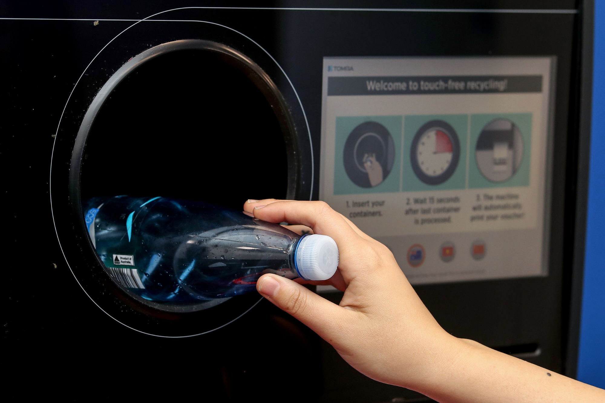 Plastic bottle with lid on being placed into Return and Earn machine