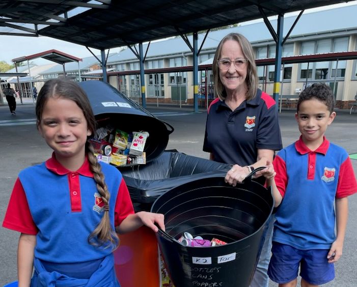 students and teachers standing beside a bin with the containers