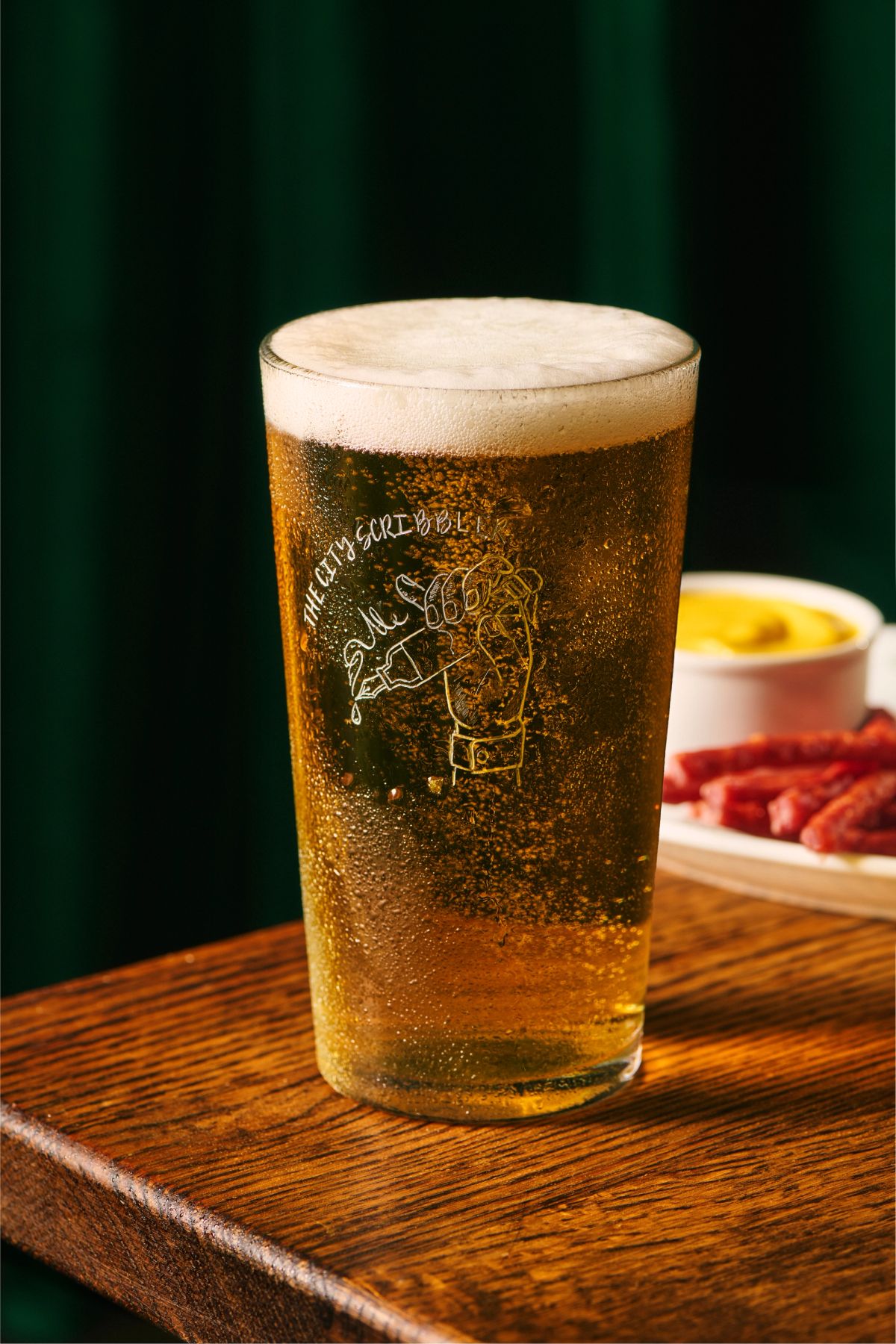 A beautifully poured pint of lager with bar snacks featured in the background