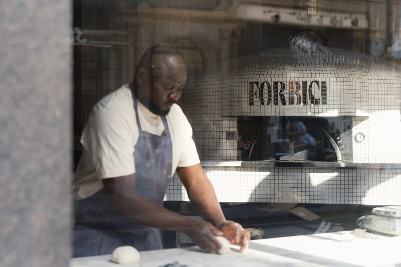 Chef rolling dough in front of pizza oven