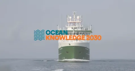 A research vessel navigating the open ocean under a clear sky.