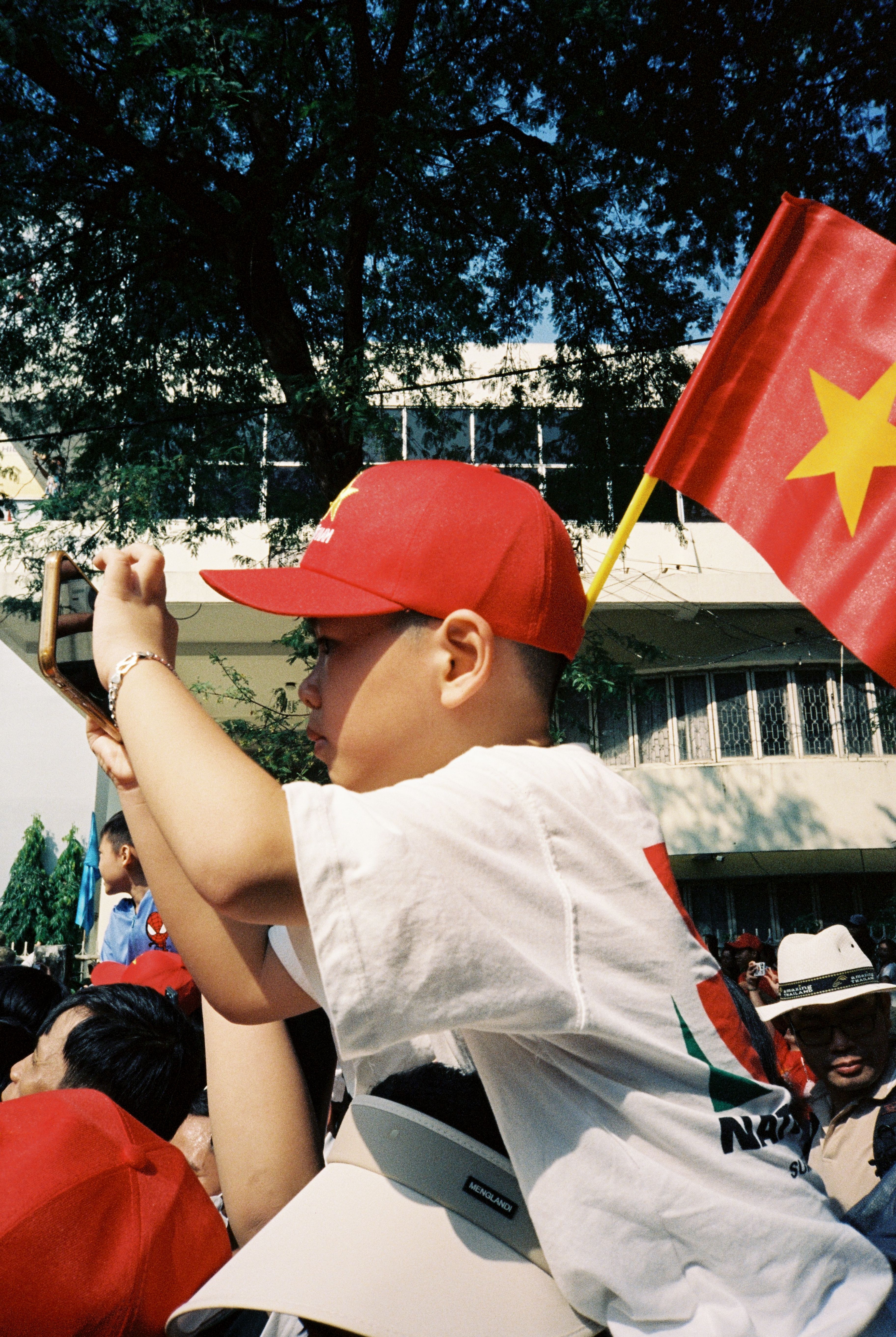 boy on shoulders holding a phone taking a picture wearing vietnam hat and flag