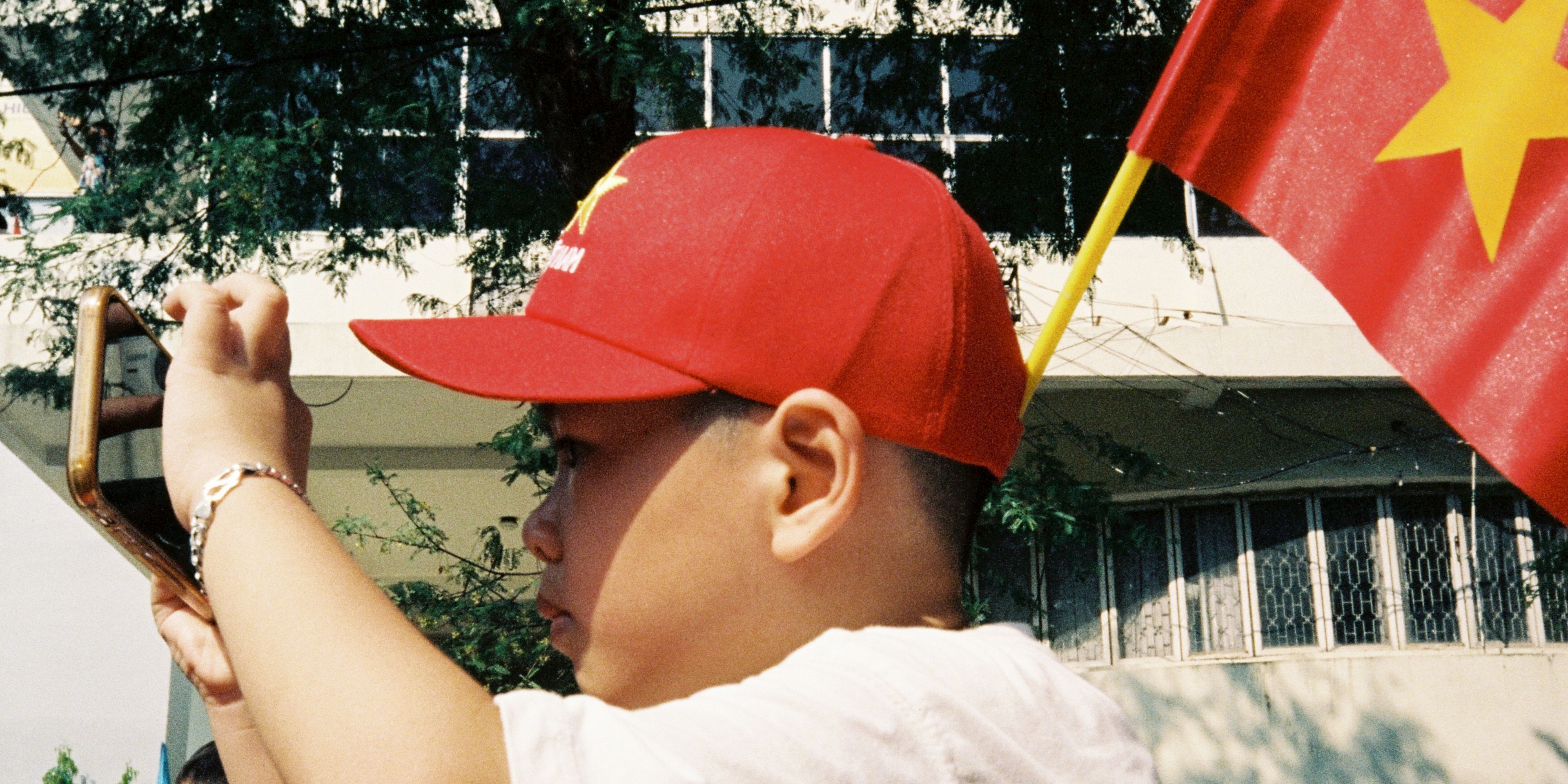 boy on shoulders holding a phone taking a picture wearing vietnam hat and flag