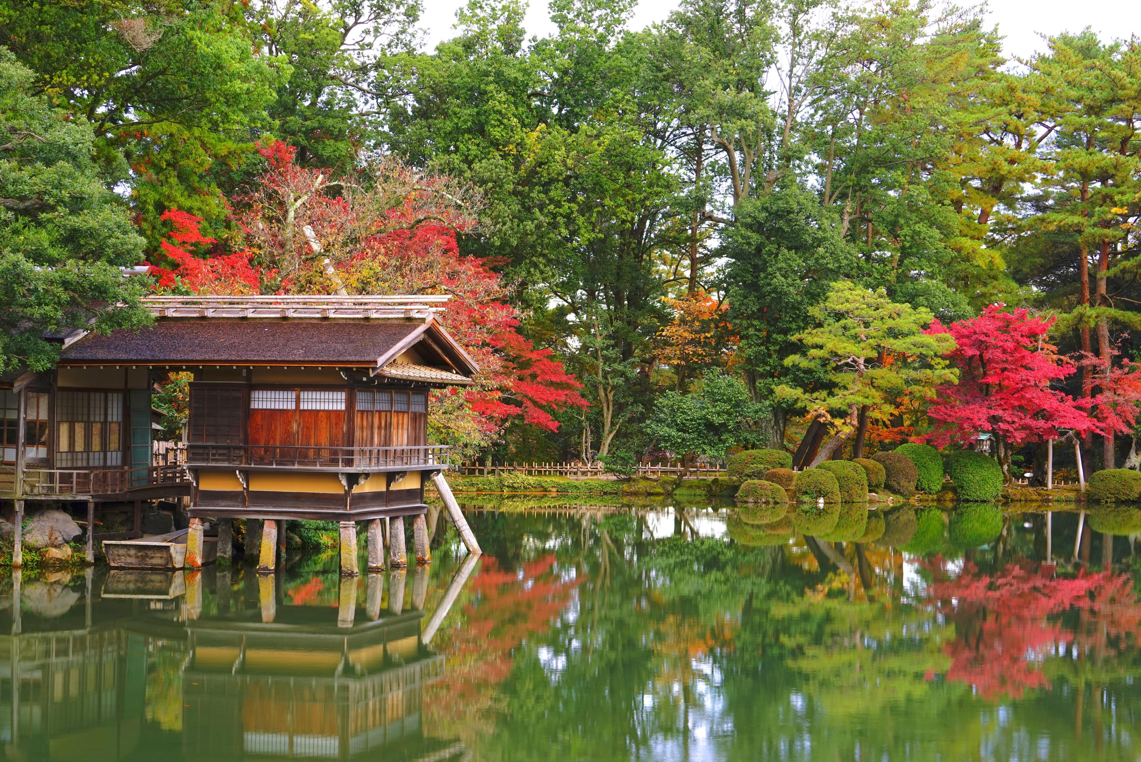 Fiery autumn foliage and sculpted trees frame a historic teahouse reflected in the calm waters of Kanazawa’s Kenroku-en Garden.