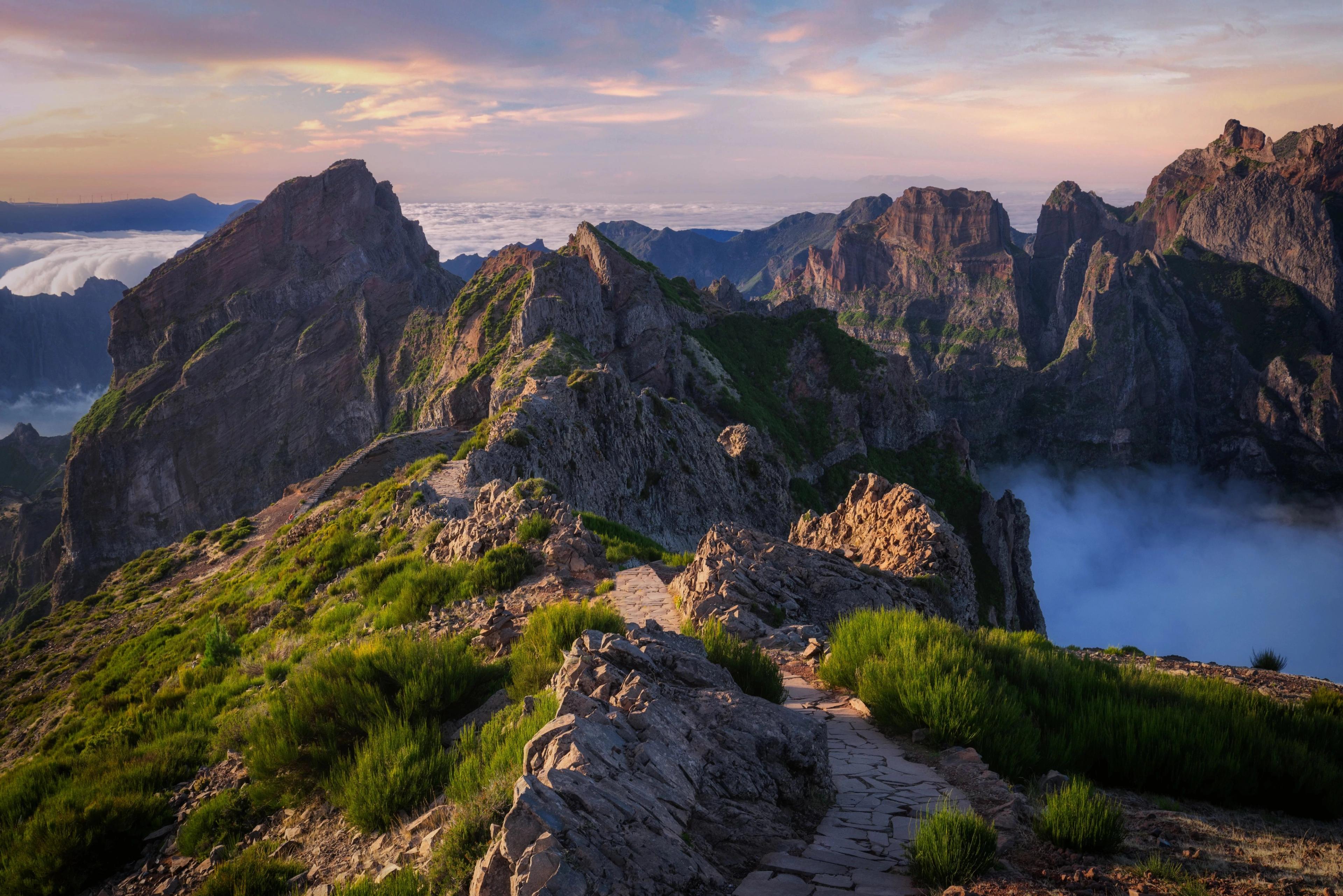 A stone pathway winds along rugged Madeira mountain peaks above a sea of clouds. 