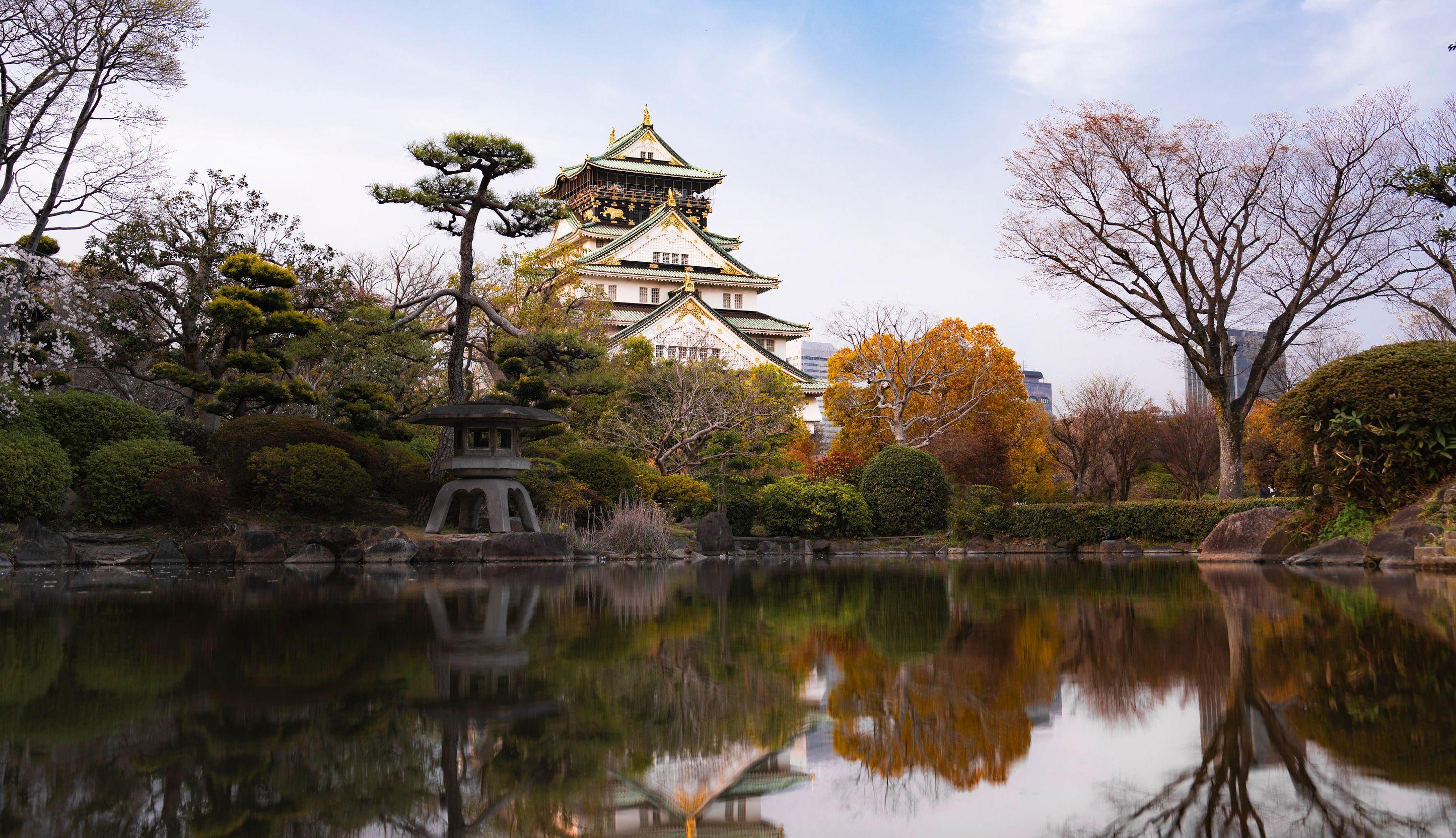 Osaka Castle and surrounding autumn foliage are reflected in a tranquil garden pond.