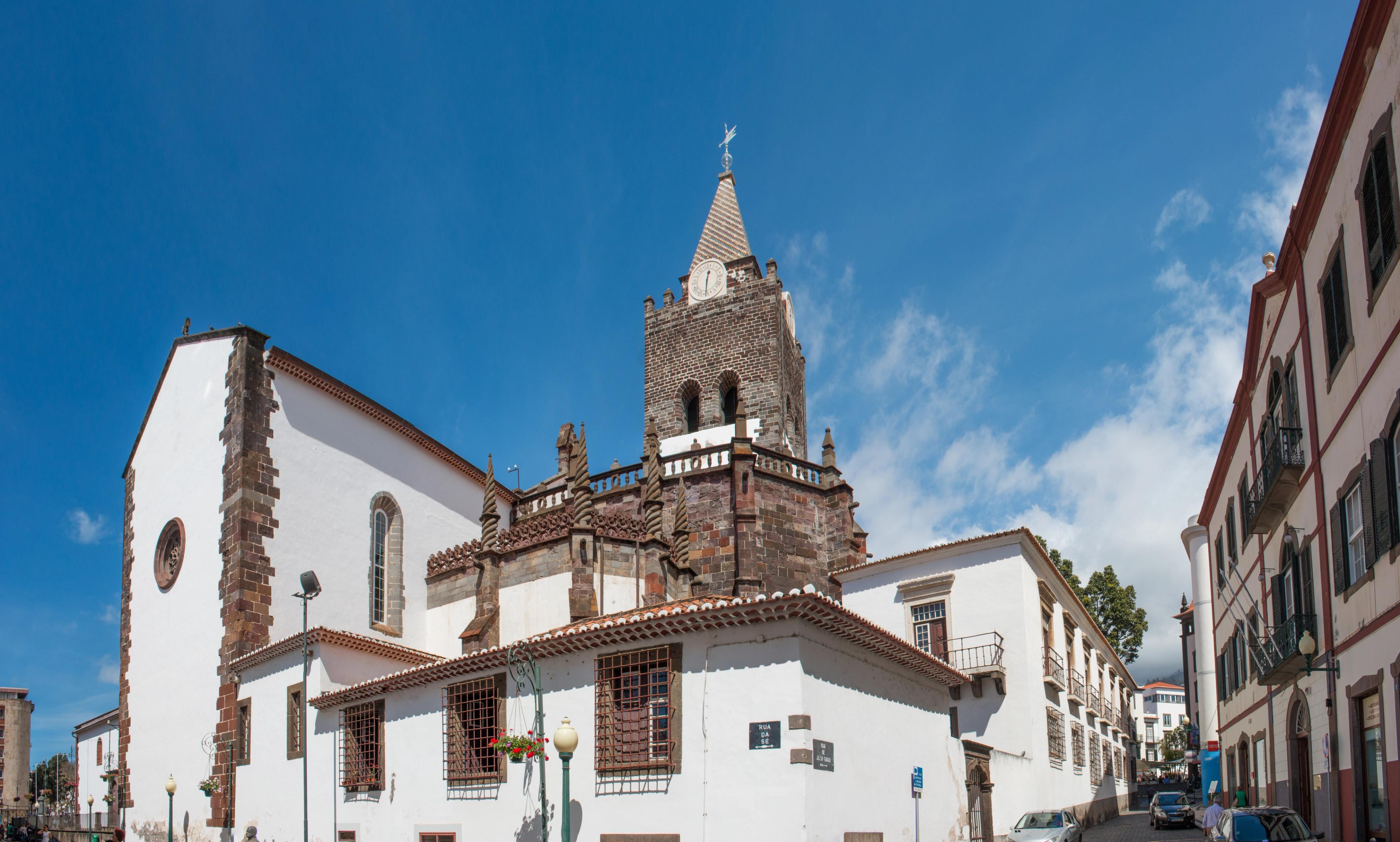 Sé Cathedral’s dark stone bell tower rises above white walls into a blue sky.
