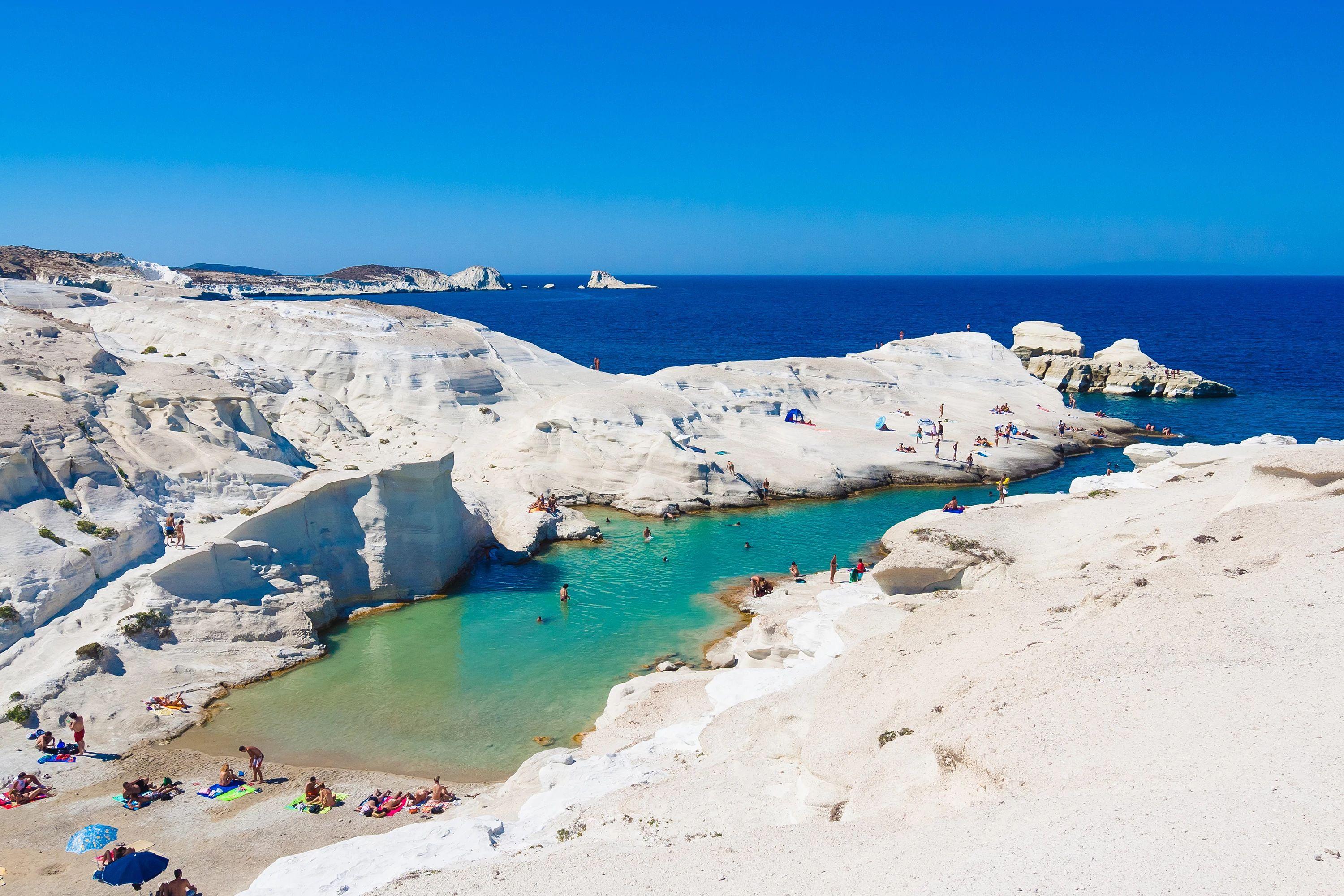 Milos Sarakiniko Beach volcanic white rock formations framing bright turquoise swimming cove water.