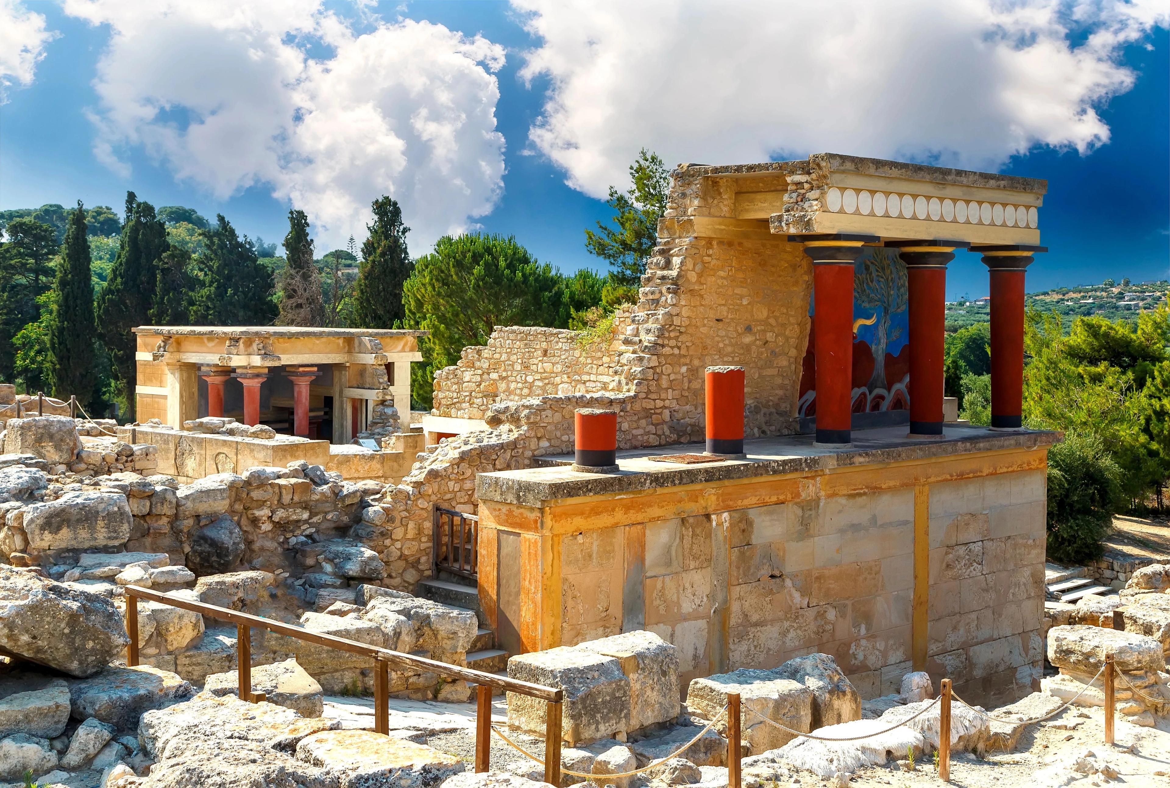 Knossos Palace ancient Minoan ruins displaying distinctive red stone columns under bright blue skies. 