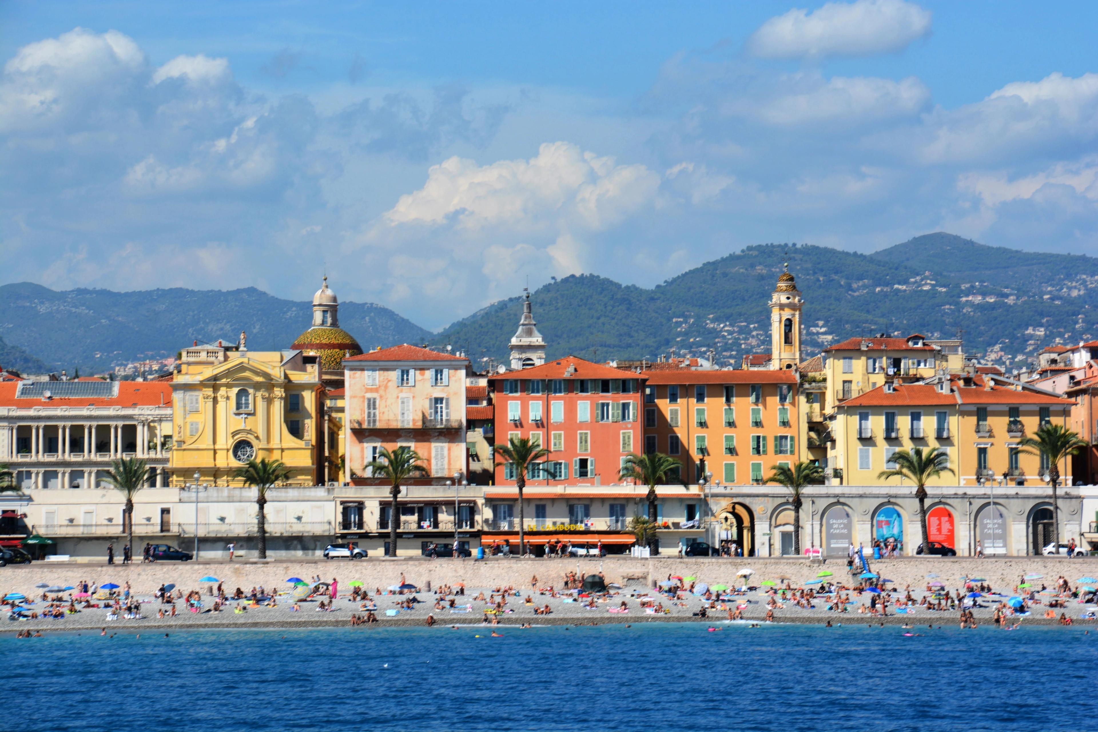 Nice Promenade des Anglais stone beach showcasing sunbathers along pastel-colored coastal buildings. 