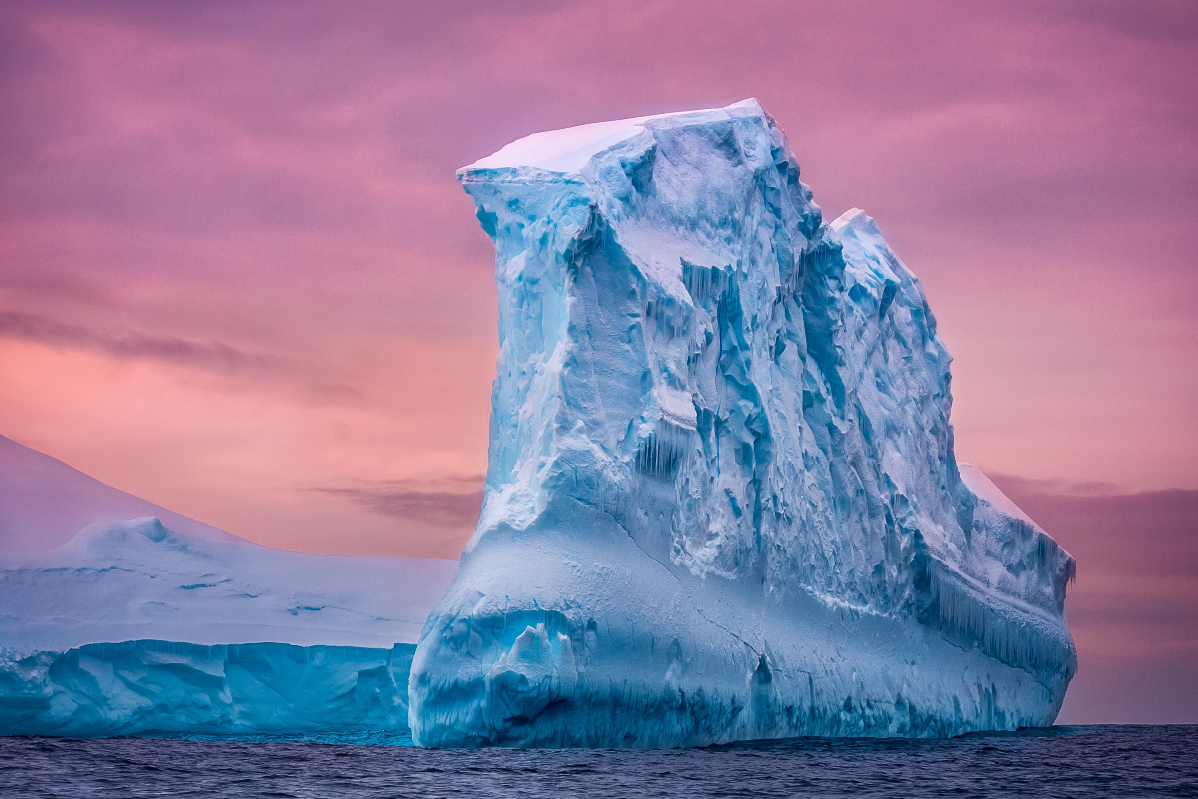Iceberg floating in the open ocean colored by pink sunset.