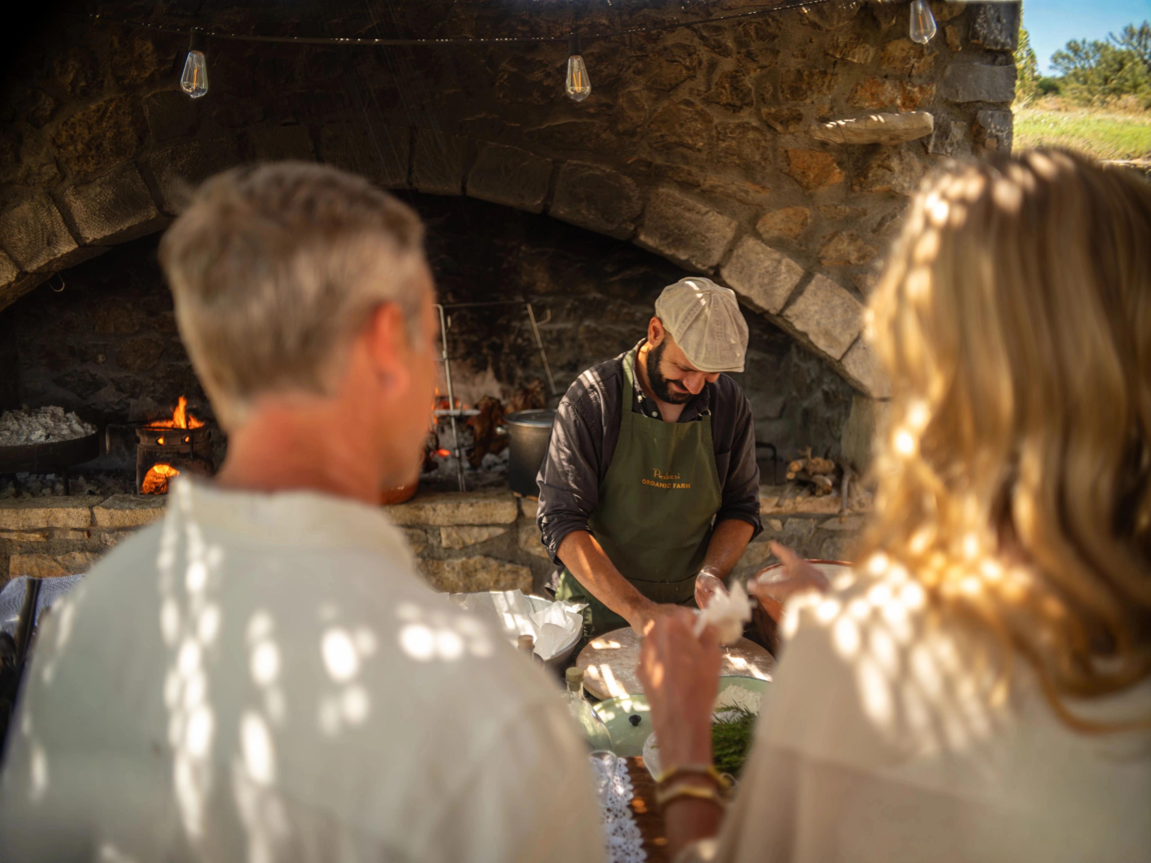 Greek tour chef shapes fresh dough, showcasing a large stone oven fireplace