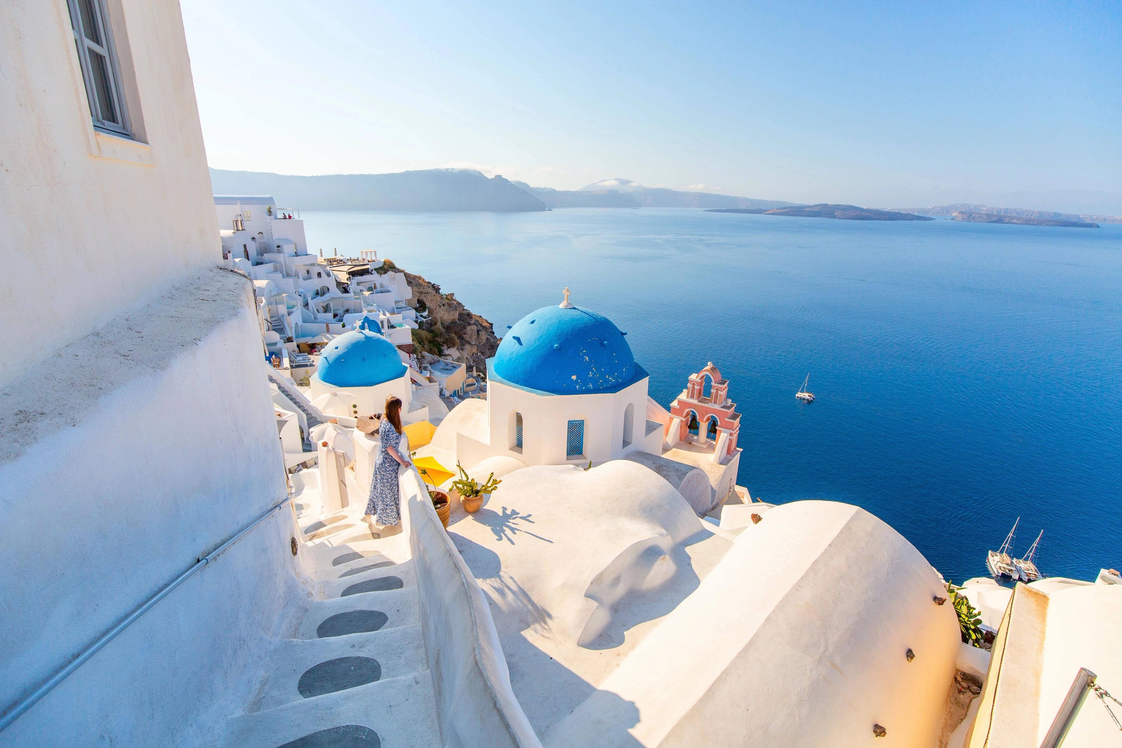 Santorini woman viewing iconic whitewashed cliffside houses framing deep blue Mediterranean waters. 