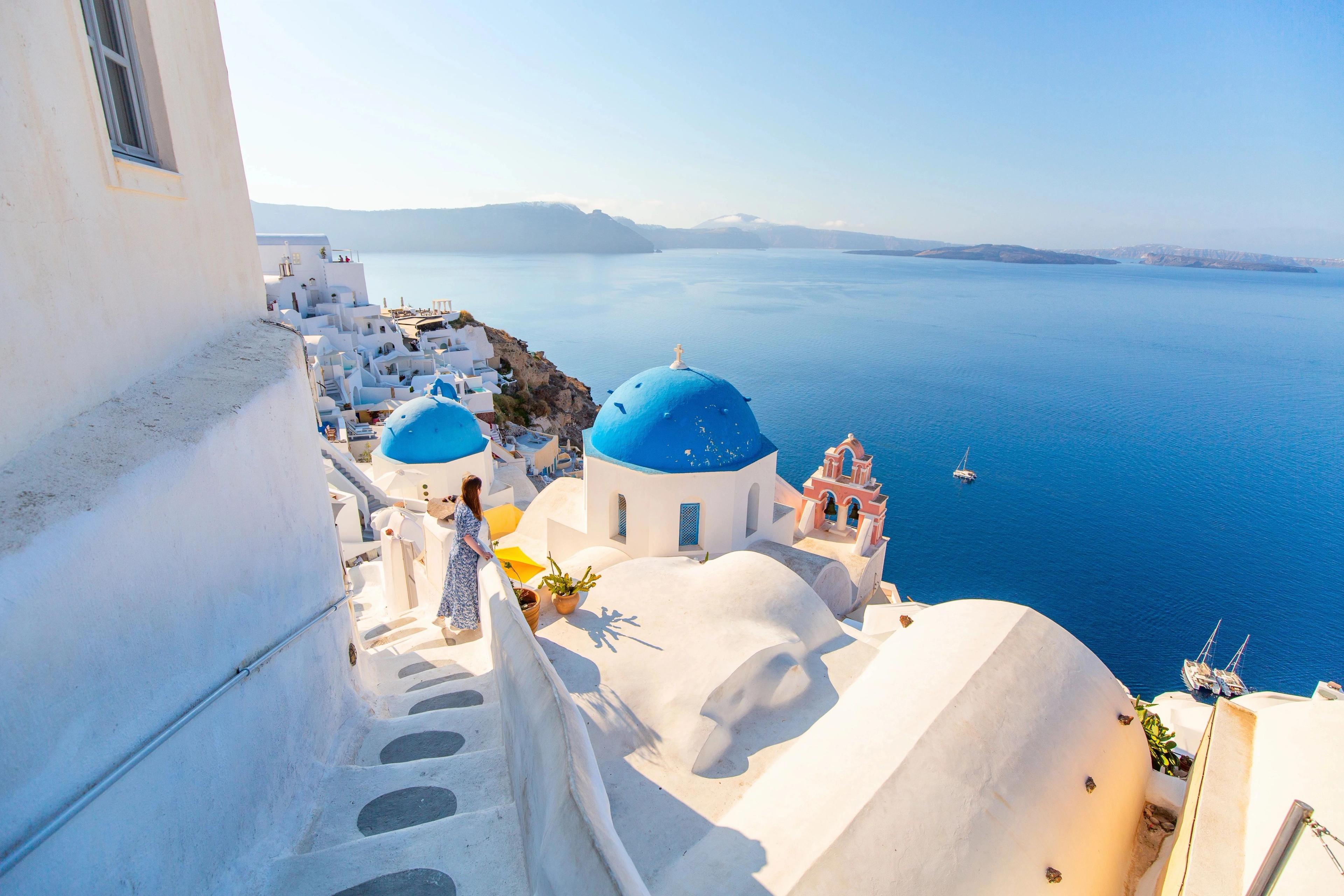 Santorini woman viewing iconic whitewashed cliffside houses framing deep blue Mediterranean waters.
