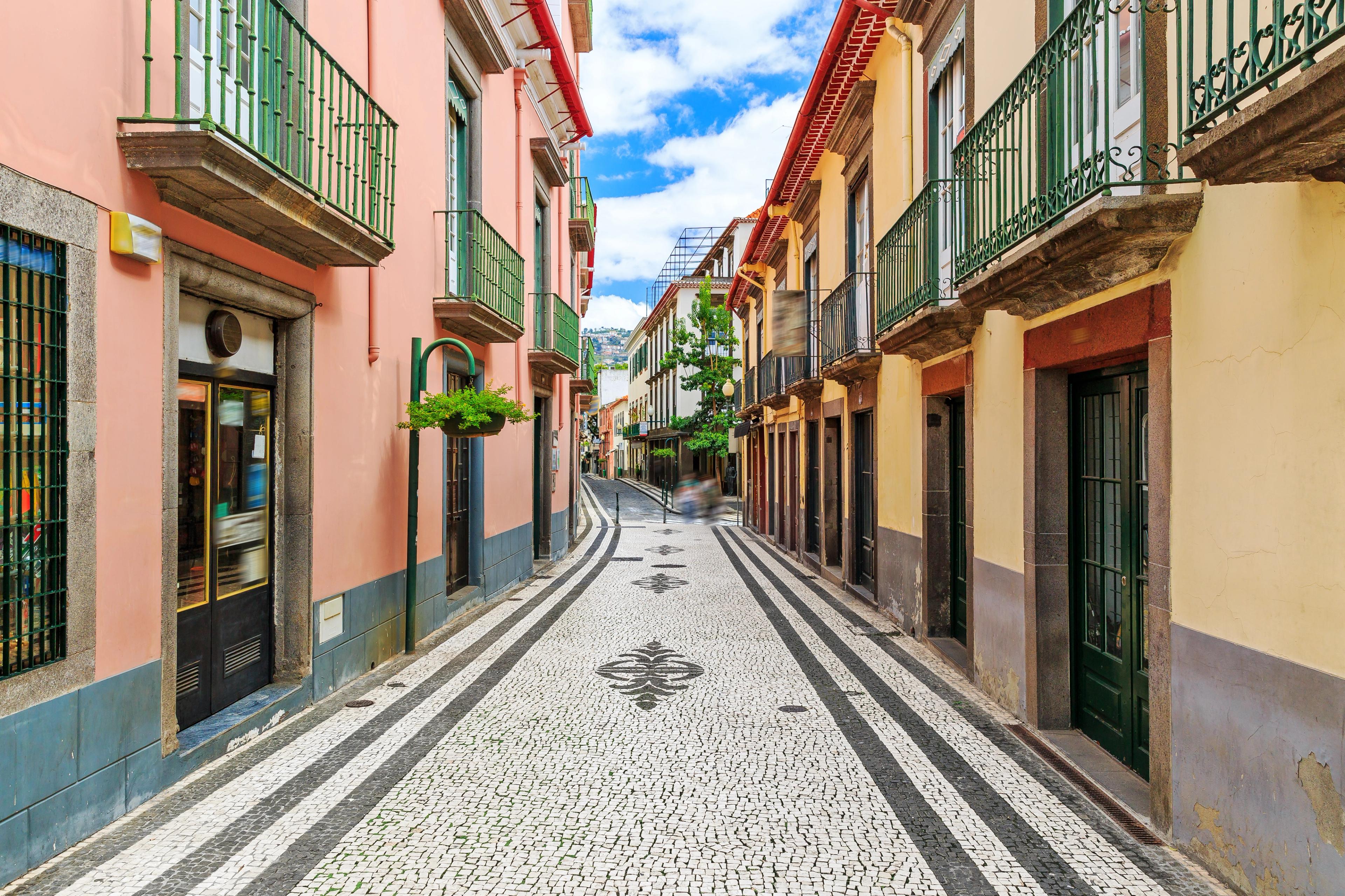 Ornate black-and-white patterned pavement lines a narrow street of colorful buildings in Funchal.