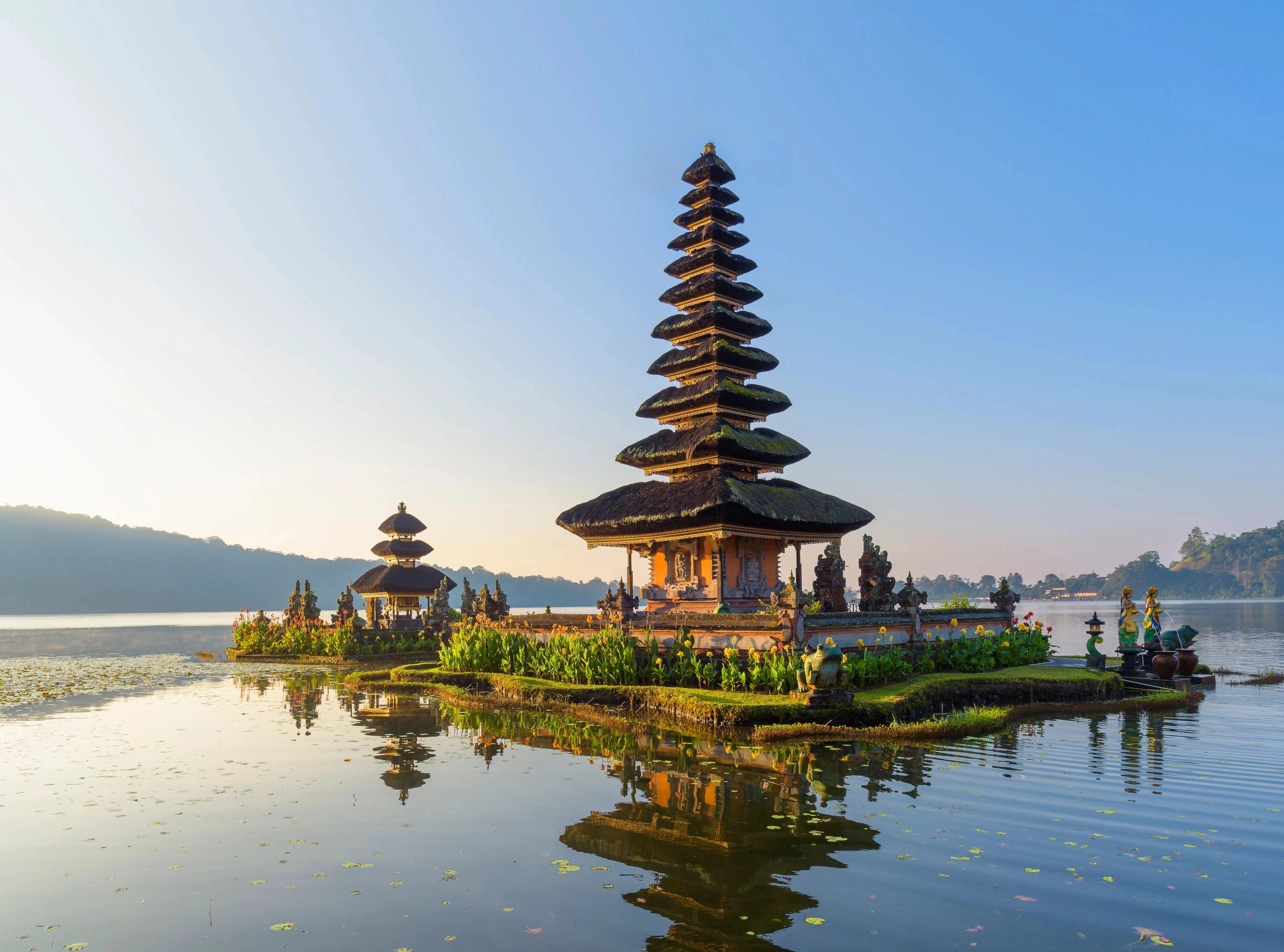 Balinese temple structure standing serenely above calm lake waters, welcoming cultural cruise excursions. 