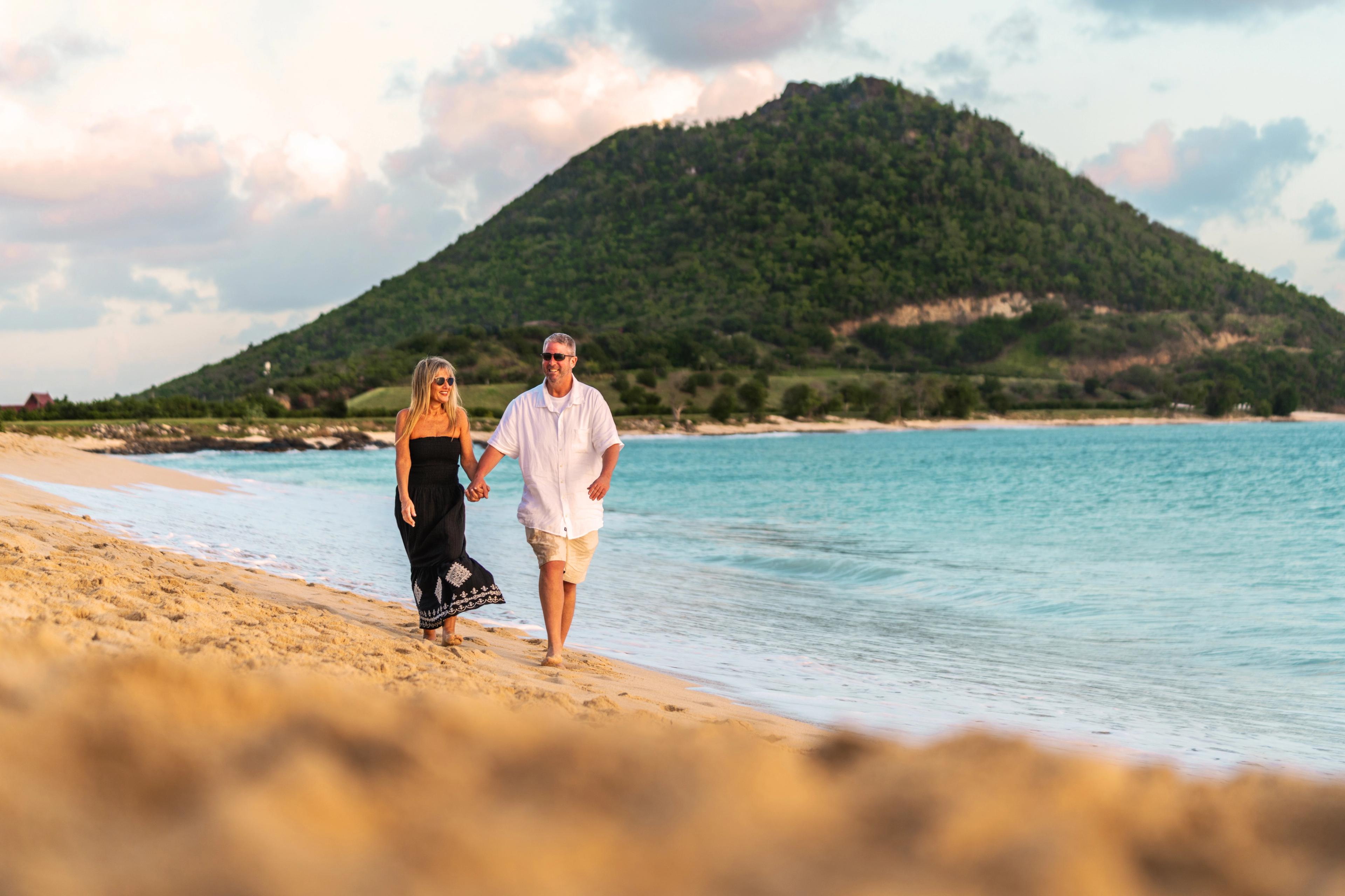 A couple strolling along Canouan Island at St. Vincent and the Grenadines with the signature Conical Hill as the backdrop.