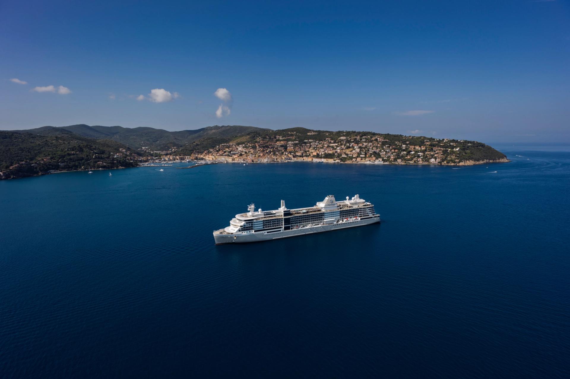 A Silversea ship anchored in a deep blue bay off a hillside town in the Mediterranean