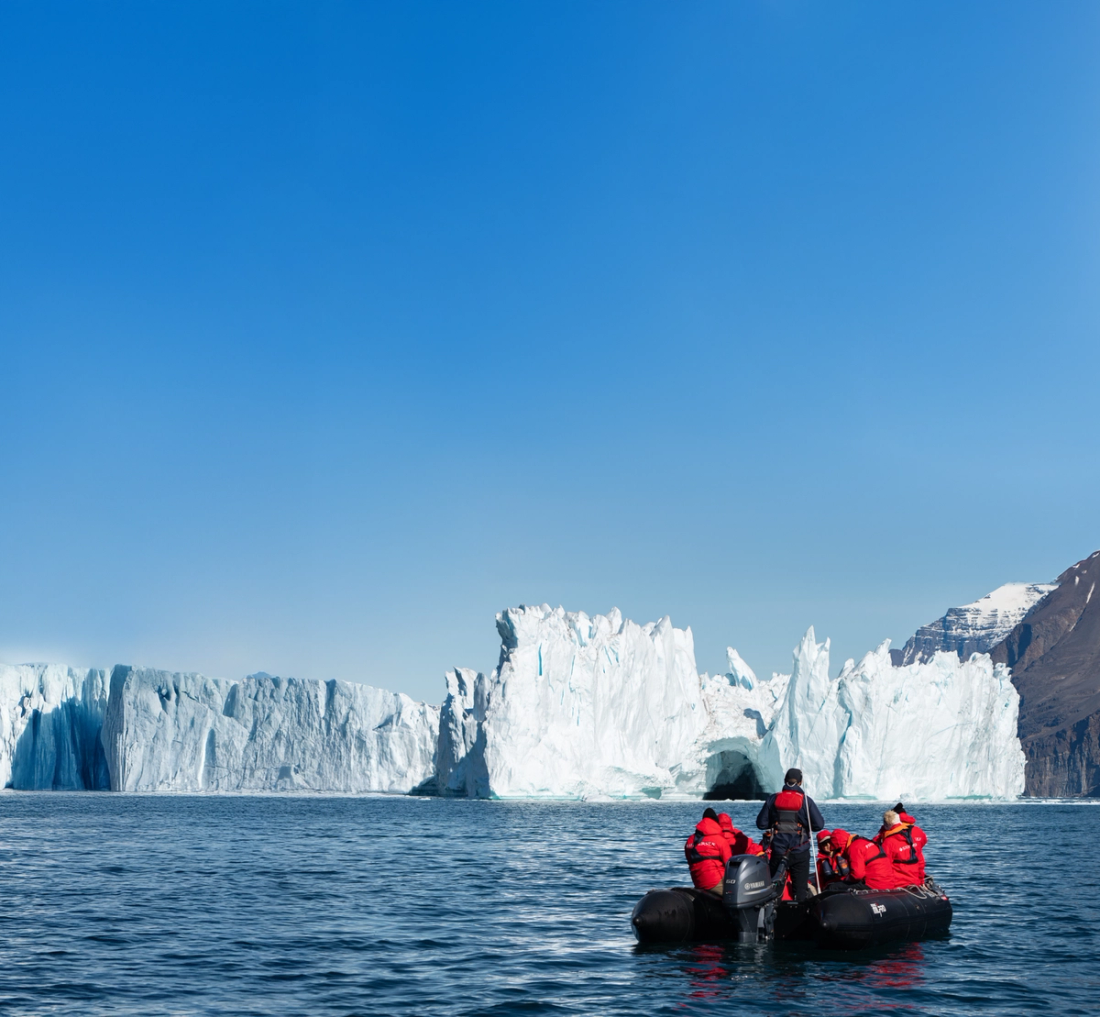 Guests in red parkas on a Zodiac beside a glacier front in the Arctic