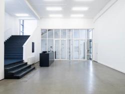 Ein heller weißer Raum, mit schwarzer Treppe und Tresen, sowie einem Screen. Der Eingangsbereich hinter der Glastür