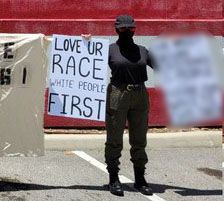 Une photo d'une personne portant tous les vêtements noirs tenant une pancarte qui dit 'Love UR ​​race white people first'.