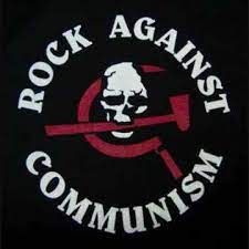 Le logo Rock Against Communism. Il comporte le texte "ROCK CONTRE LE COMMUNISME" entourant un crâne qui mord dans un marteau et une faucille.
